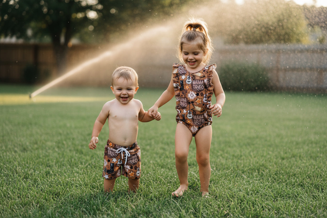 girl and boy running through sprinkler wearing mama tried brown western sibling swimsuits