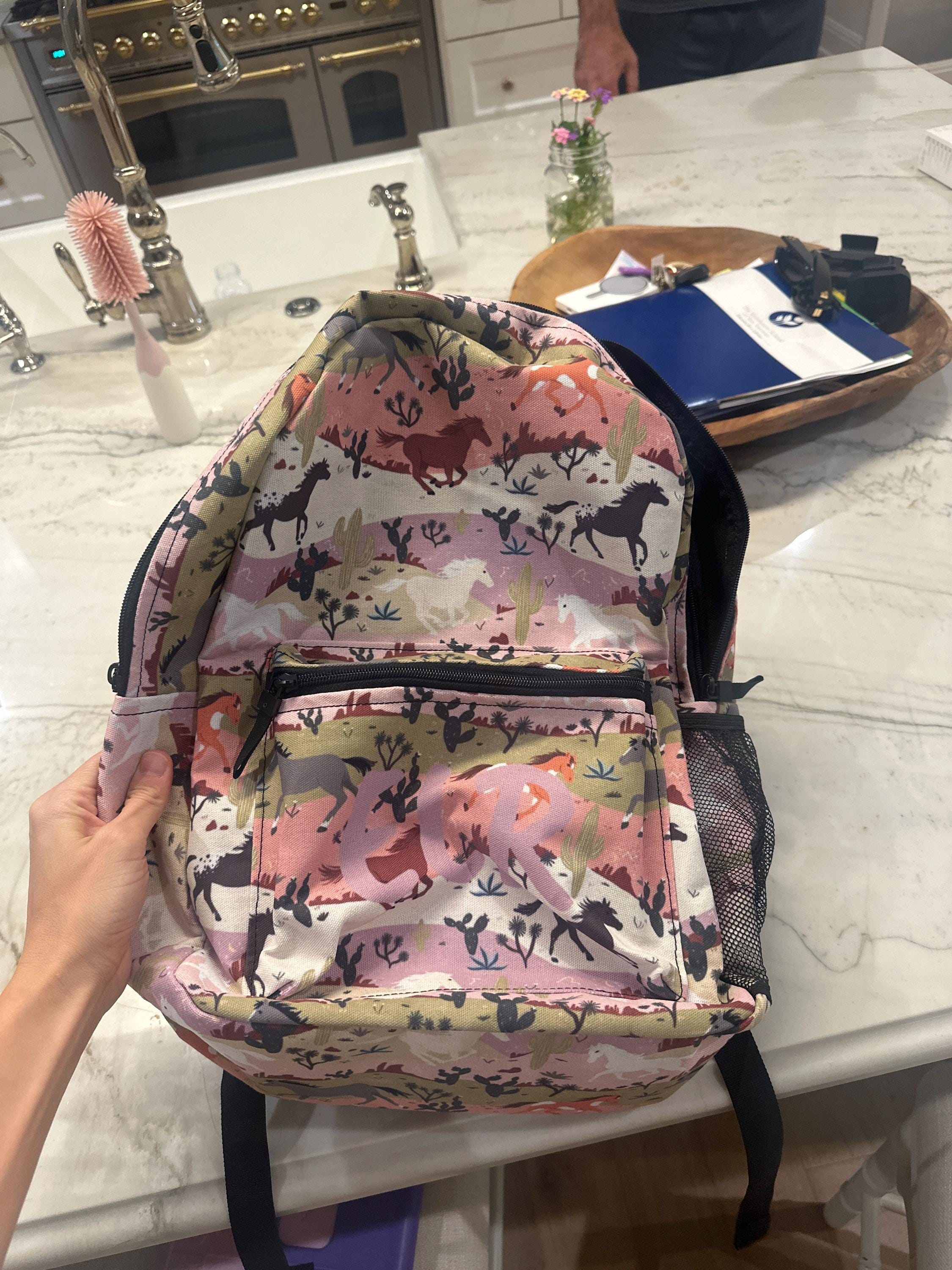 Backpack with horse pattern held by a hand on a kitchen counter.