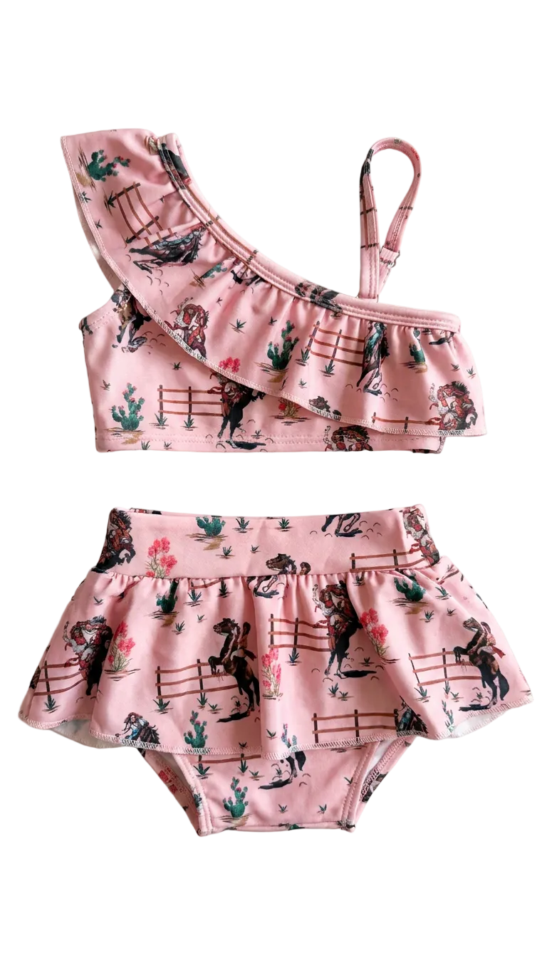 Pink children's two-piece tankini swimsuitt with cowgirls, horses and cacti design on a white background