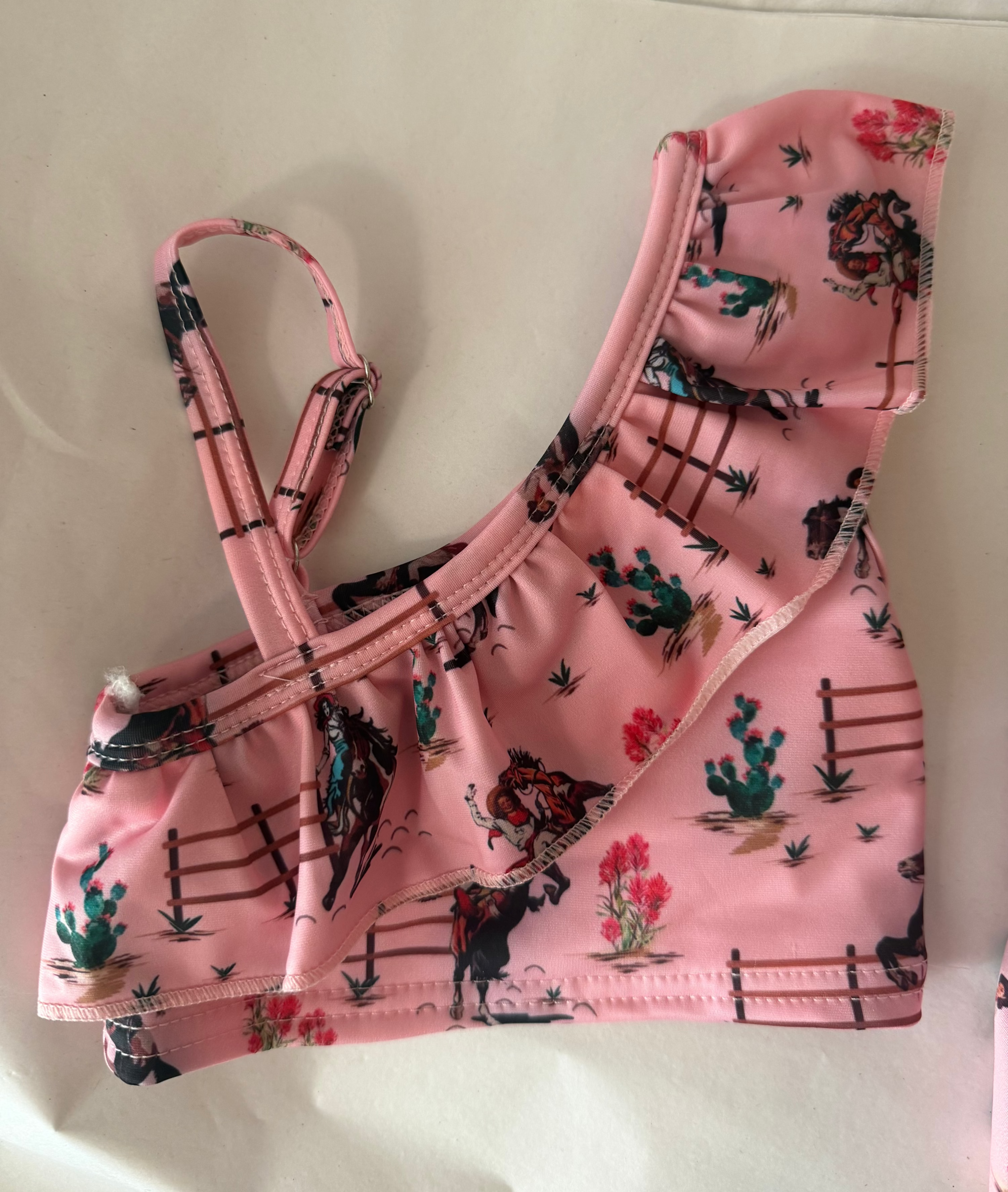 vintage cowgirls pink tankini top against white background features an adjustable shoulder strap and ruffled shoulder and neckline
