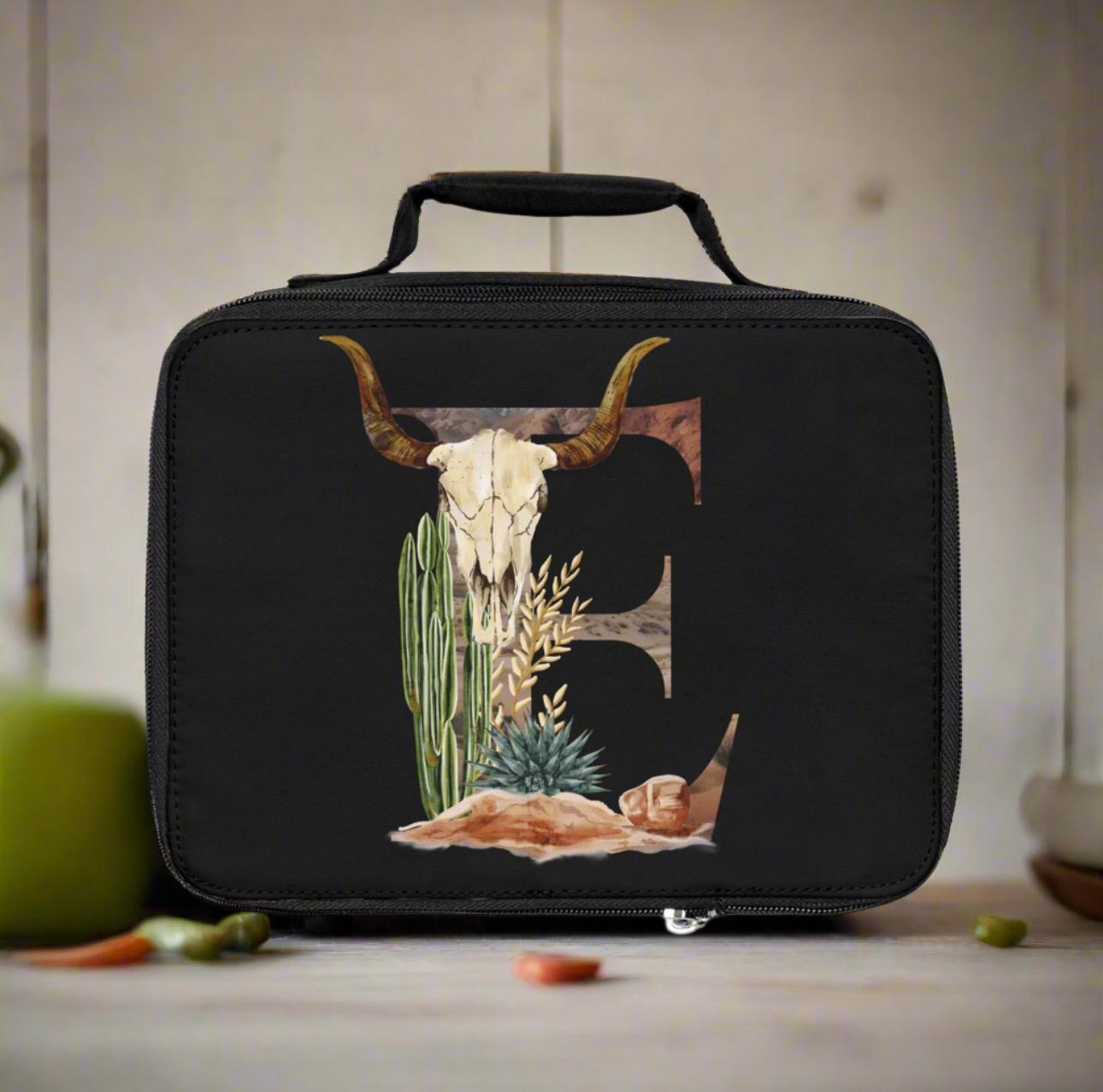 Black insulated lunch bag with a bull skull and cactus design on a wooden surface.