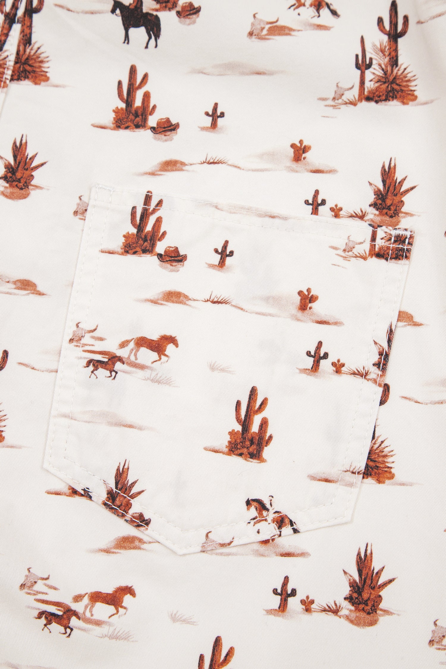 close up of womens western jumpsuit Fabric with desert-themed pattern featuring cacti, horses, and other elements on a white background