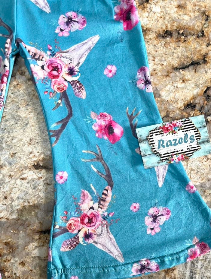 CLOSEUP OF Turquoise PANTS with floral and antler design on a stone surface, featuring a brand tag.