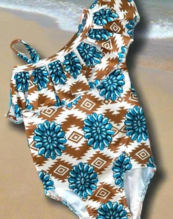 Cowgirl Swimsuit, Turquoise Conchos, Western Swimsuits, SOUTHWESTERN, Squash blossoms, Girls One piece swim, Ruffle Swimsuit, Girls' Western Swimsuit  Two of our favorite things – Aztec prints and turquoise concho squash blossoms – come together in this stunning Western-inspired swimsuit! 😍 This girls' one-piece ruffle swimsuit is a must-have for little cowgirls who love bold, Southwestern style. Available 0-3 months - girls 12/14. Ships FREE $35+ order from Montana.
