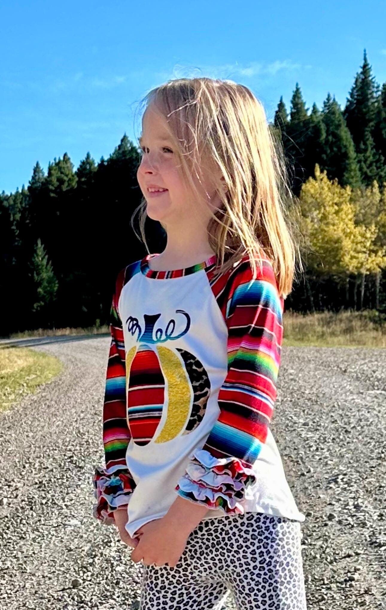 Jernie modeling Fall Stripes Pumpkin Ruffle Sleeve Shirt. This Fall Shirt features a pumpkin with Fall serape stripes, cheetah print and glitter gold. The neckline and sleeves are festive serape stripes with wrist ruffles. So cute!