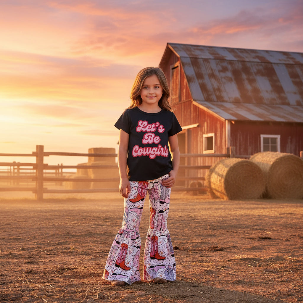 Black t-shirt with 'Let's Be Cowgirls' text and patterned pants with cowboy boot design on a textured surface.