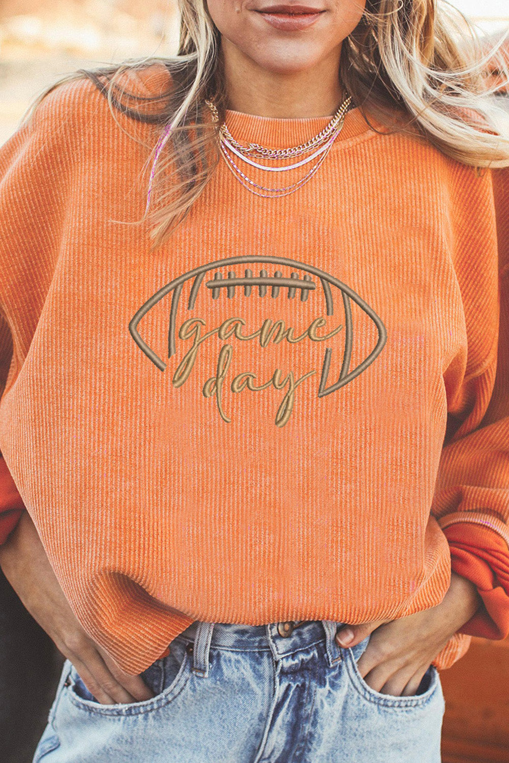 Person wearing an orange 'Game Day' sweater with a football graphic.