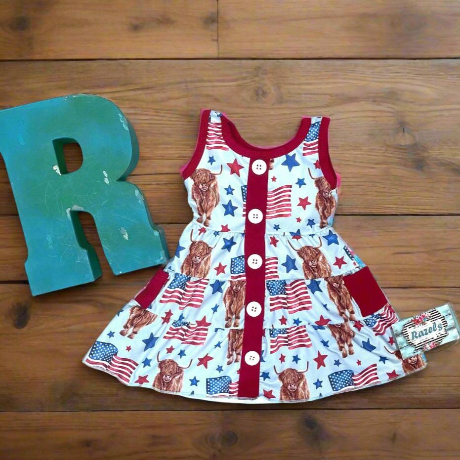 Get ready to celebrate the 4th of July in full-on Western style with our adorable Highland Cow & American Flag DRESS FEATURING A TANK TOP STYLE DRESS WITH FAUX BUTTON FRONT. PICTURED ON WOODEN BACKROUND WITH RAZELS LETTER R 