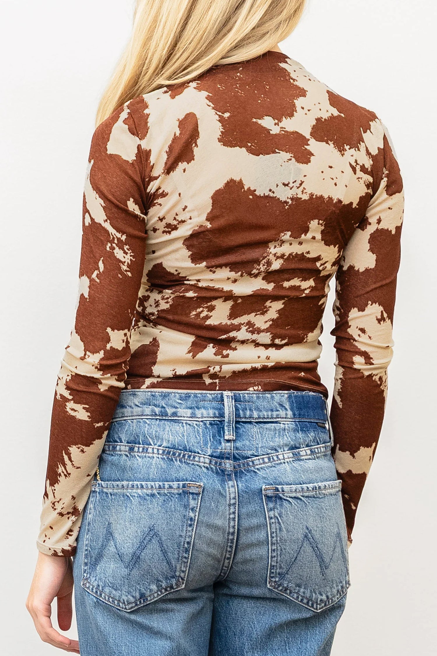 A woman viewed from the back wearing a fitted long-sleeve top with a brown and beige cow-print pattern, paired with blue jeans.
