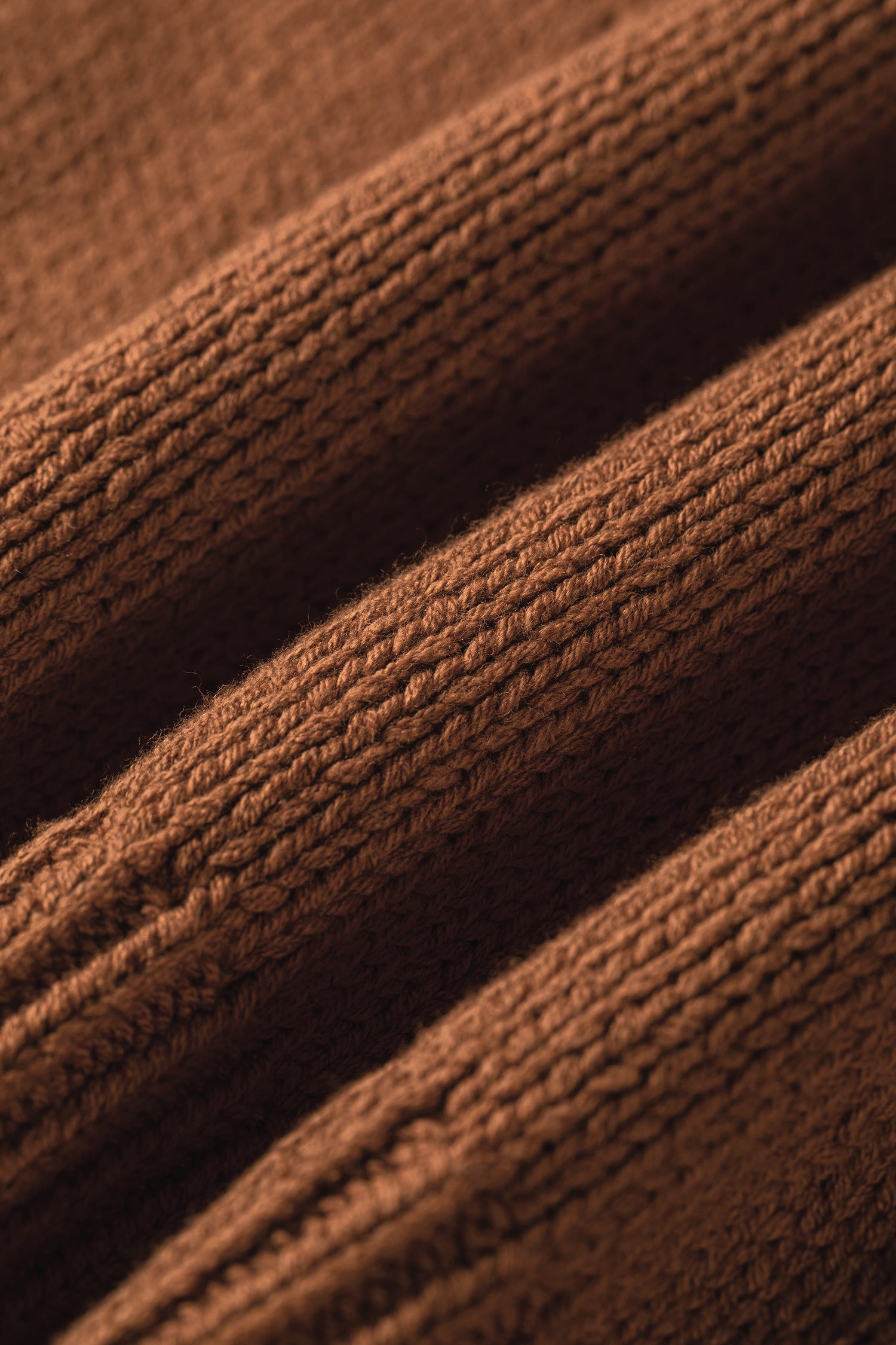 Close-up of a brown ribbed knit fabric texture with soft folds and horizontal ribbed pattern.