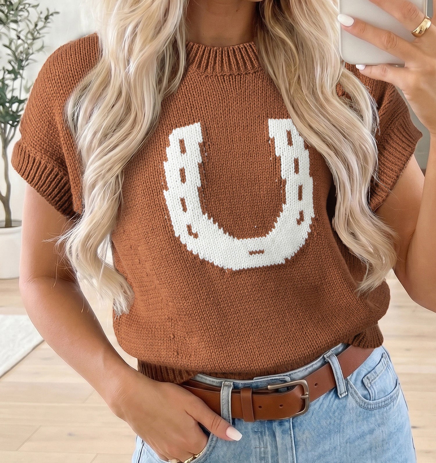 Woman wearing a brown sweater with a white horseshoe design, standing indoors.