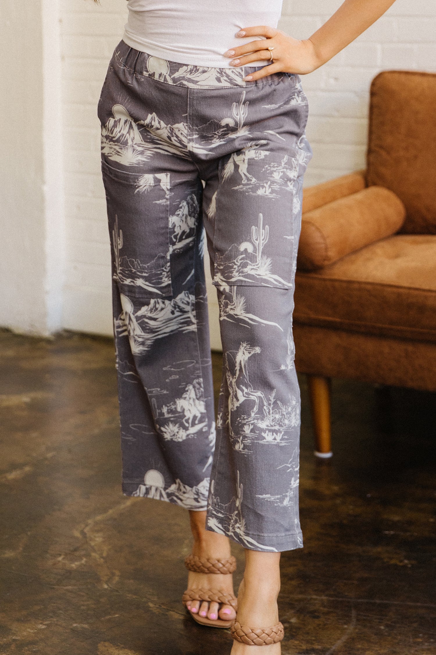 Person wearing gray patterned pants standing in a room with a brown couch.