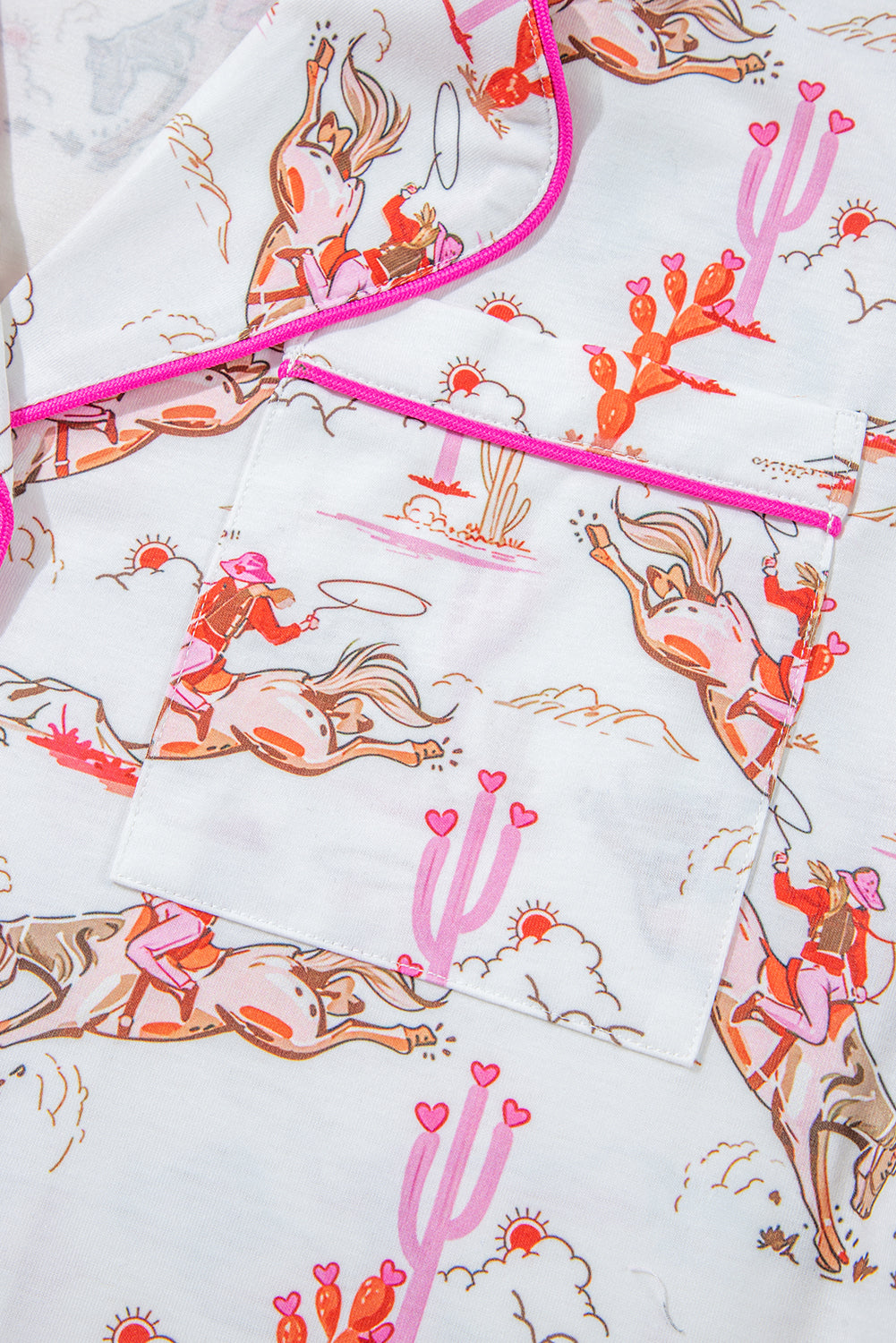 close up view of pink cowgirl pajama fabric showing cowgirls on bucking horses, pink and orange cacit, setting suns and pink piping on these western lounge set for women