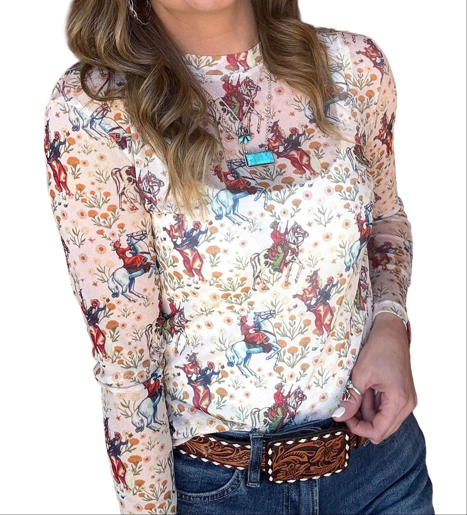 A woman wearing a long-sleeve high-neck blouse with a multicolor cowboy and cattle print on a cream background, paired with a brown tooled belt and blue jeans, against a plain white background.