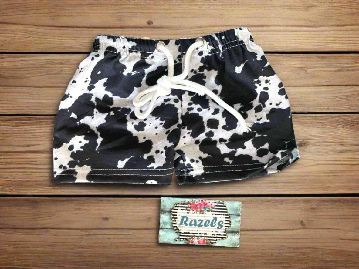 holestein cow swim trunks for boys against wooden background and razels business card