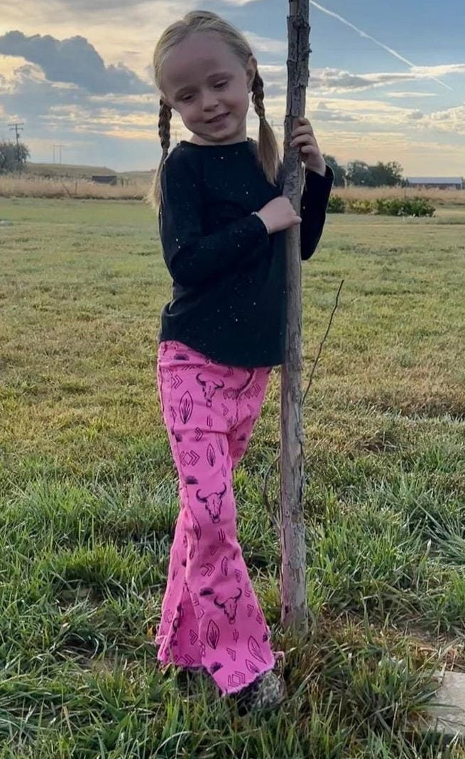Jernie modeling girls hot pink western jeans. Jeans feature black steerheads, arrows, and cacti in an awesome western motif. Jeans have an adjustable waistband, pockets, and a frayed bell bottom hem.