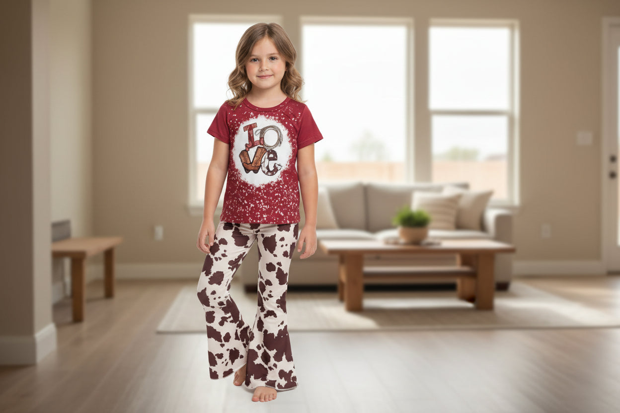 Child wearing a red t-shirt with a 'LOVE' graphic and cow print pants on a white background