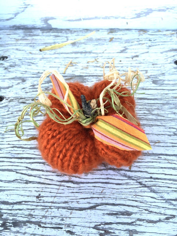 Orange hand-knit pumpkin decoration. Pumpkins have sticks, raffia and fabric leaves, and vines.