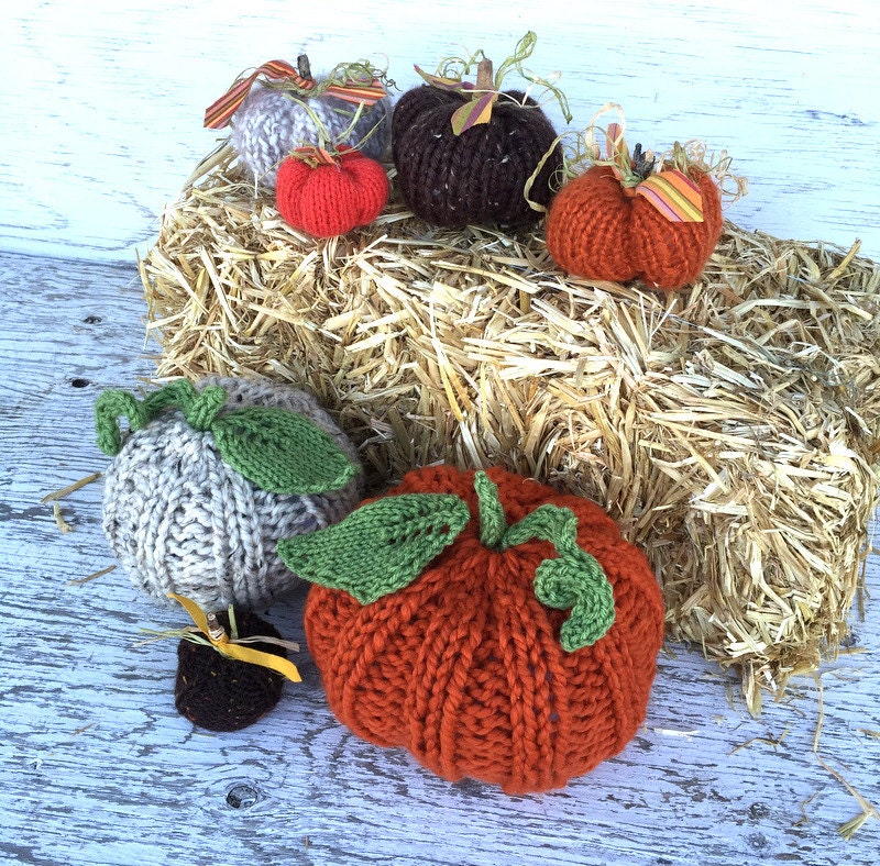 group of handknit pumpkins in various sizes. Large pumpkins have handknit vines and leaves, smaller pumpkins have decorative vines and leaves made from sticks, fabric, and raffia.