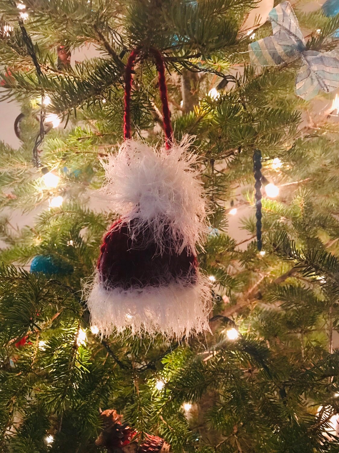 Handknit Santa Hat Christmas Tree Decoration. Hat is red with a fluffy white border/brim and white pom pom