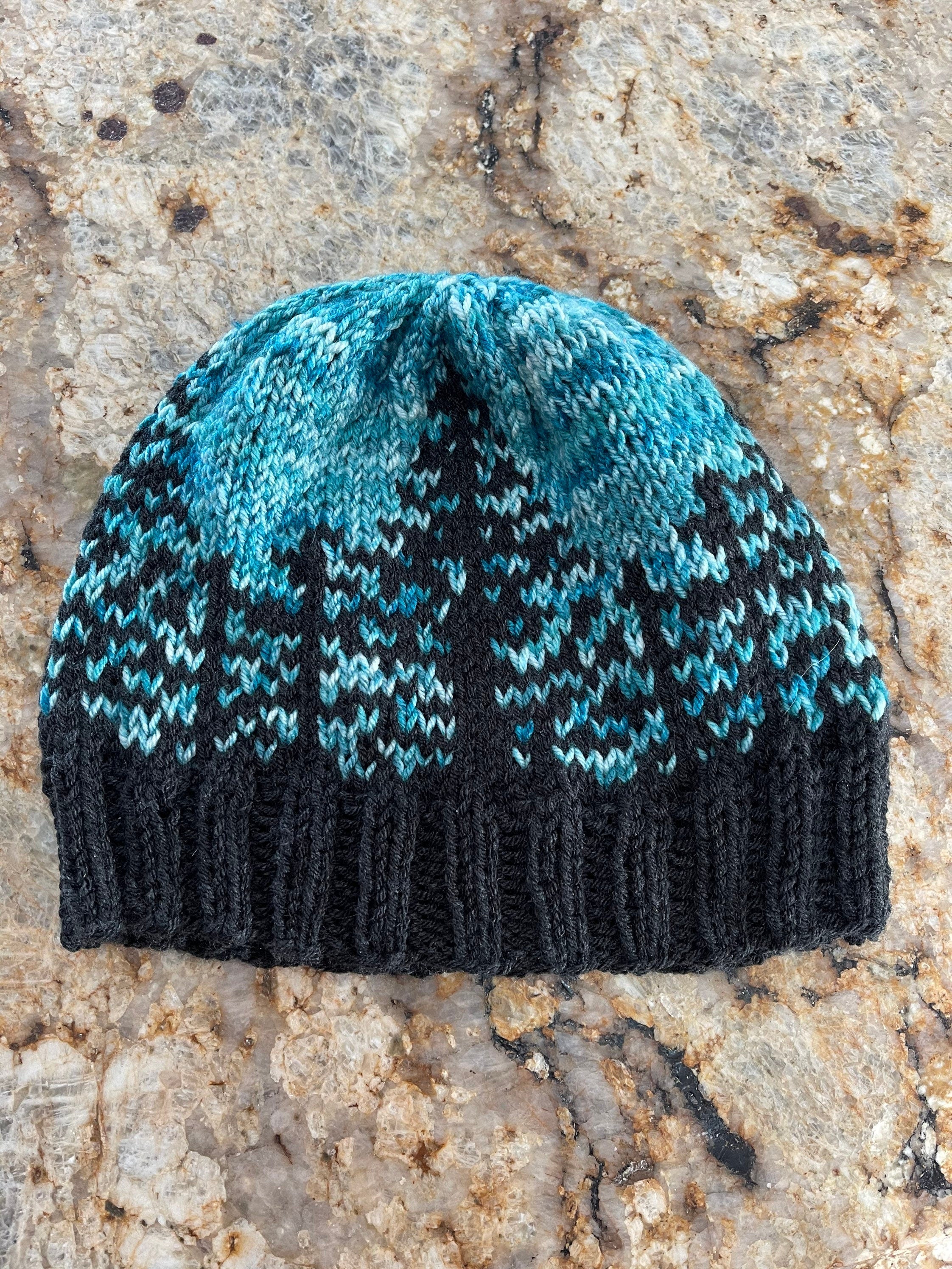 Handknit hat featuring a charcoal grey brim and a forest of trees. The background is beautiful turquoise. This hat is ready to ship and a size large.