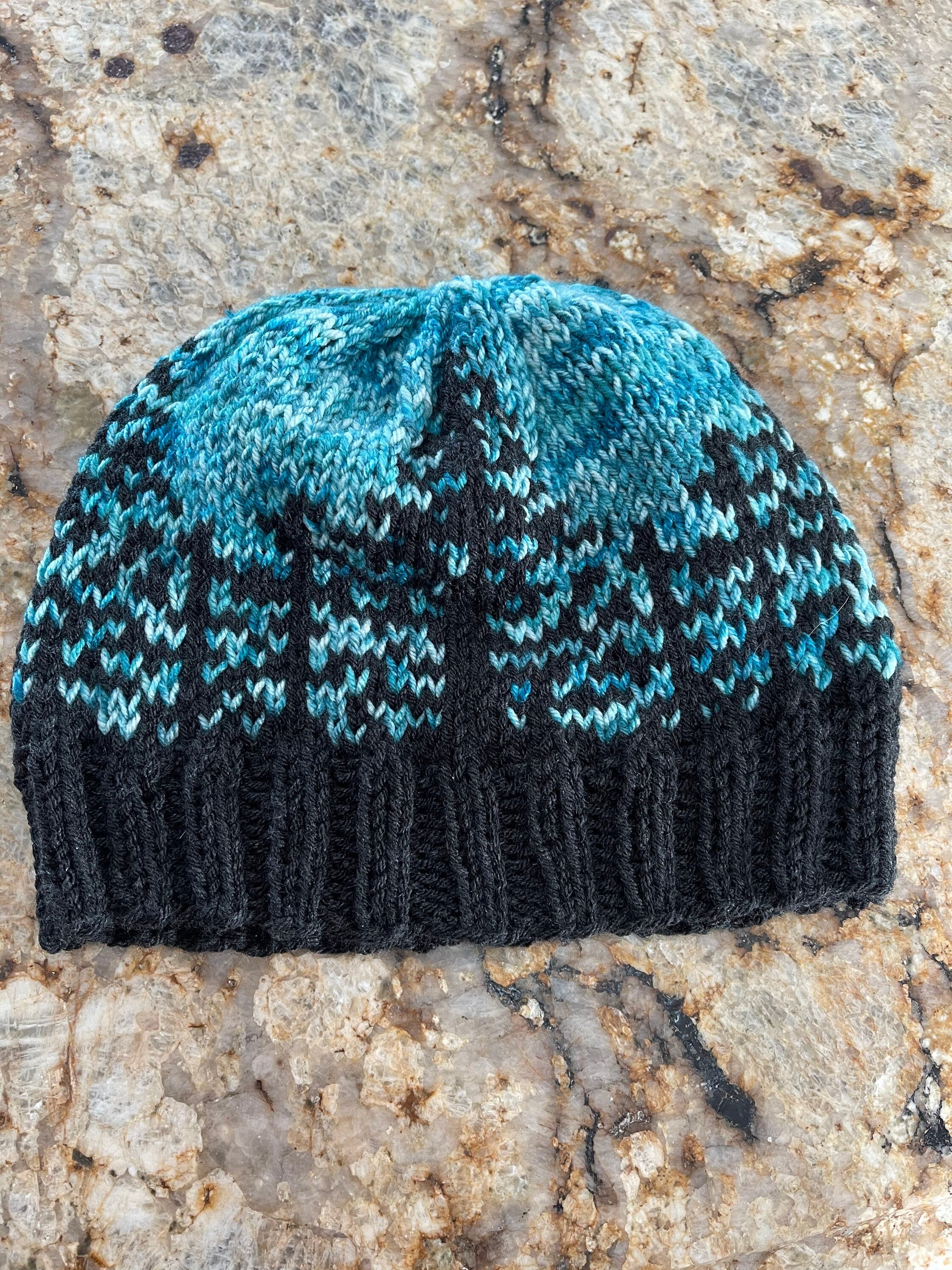 Handknit hat featuring a charcoal grey brim and a forest of trees. The background is beautiful turquoise. This hat is ready to ship and a size large.