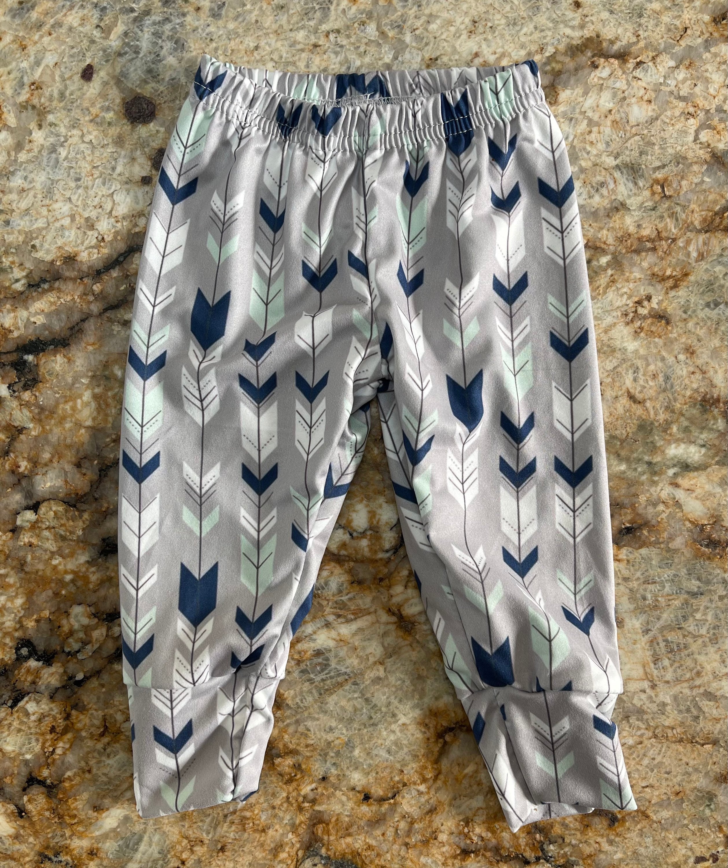 Wild One Jogger Set for Kids! Featuring a bold arrow print on the jogger pants in shades of grey, white, blue, and mint, this set is paired with a striking blue t-shirt that proudly displays &quot;WILD&quot; down the front. Ships FREE with $35+ purchase