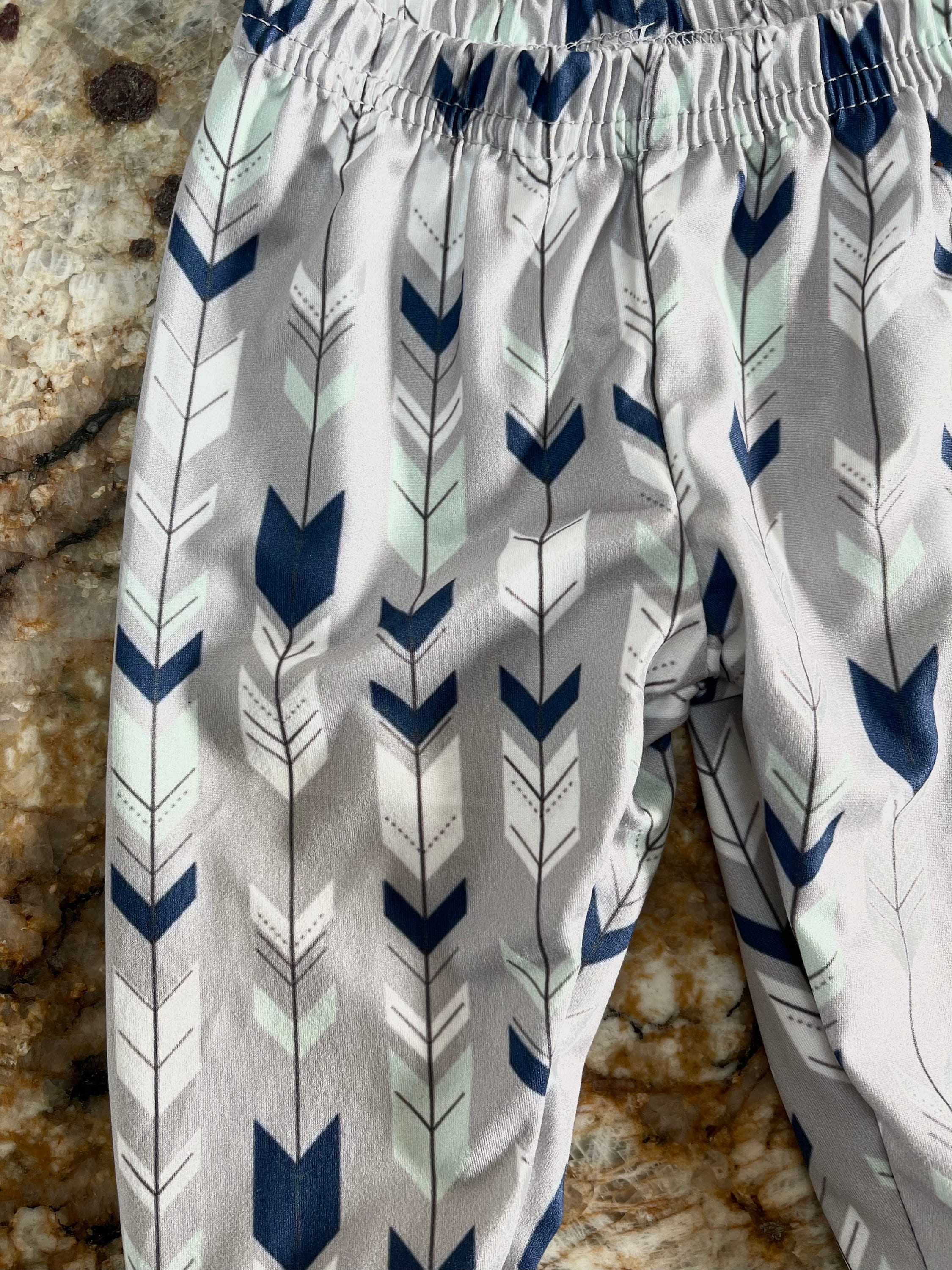 Wild One Jogger Set for Kids! Featuring a bold arrow print on the jogger pants in shades of grey, white, blue, and mint, this set is paired with a striking blue t-shirt that proudly displays &quot;WILD&quot; down the front. Ships FREE with $35+ purchase