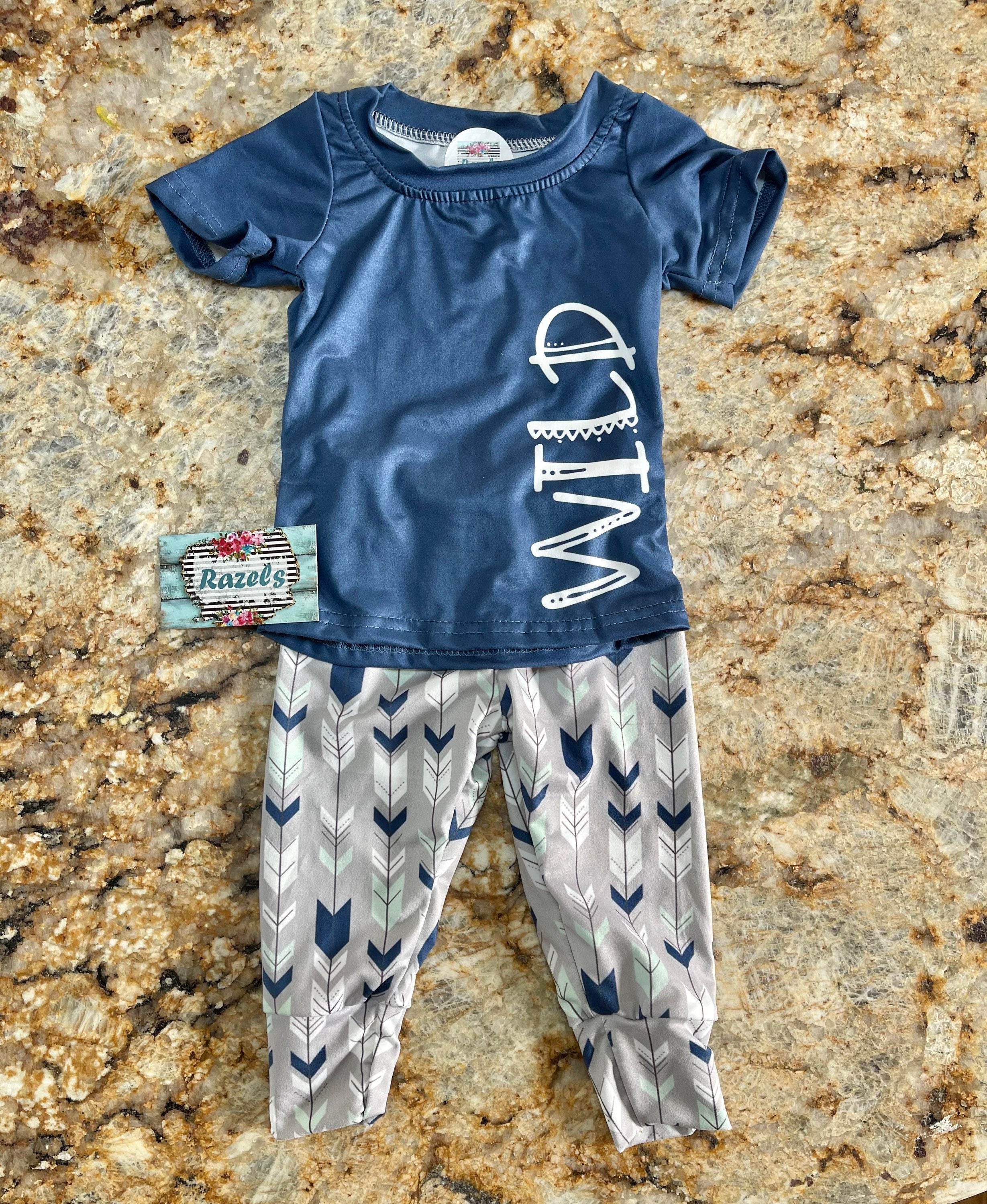 Wild One Jogger Set for Kids! Featuring a bold arrow print on the jogger pants in shades of grey, white, blue, and mint, this set is paired with a striking blue t-shirt that proudly displays &quot;WILD&quot; down the front. Ships FREE with $35+ purchase