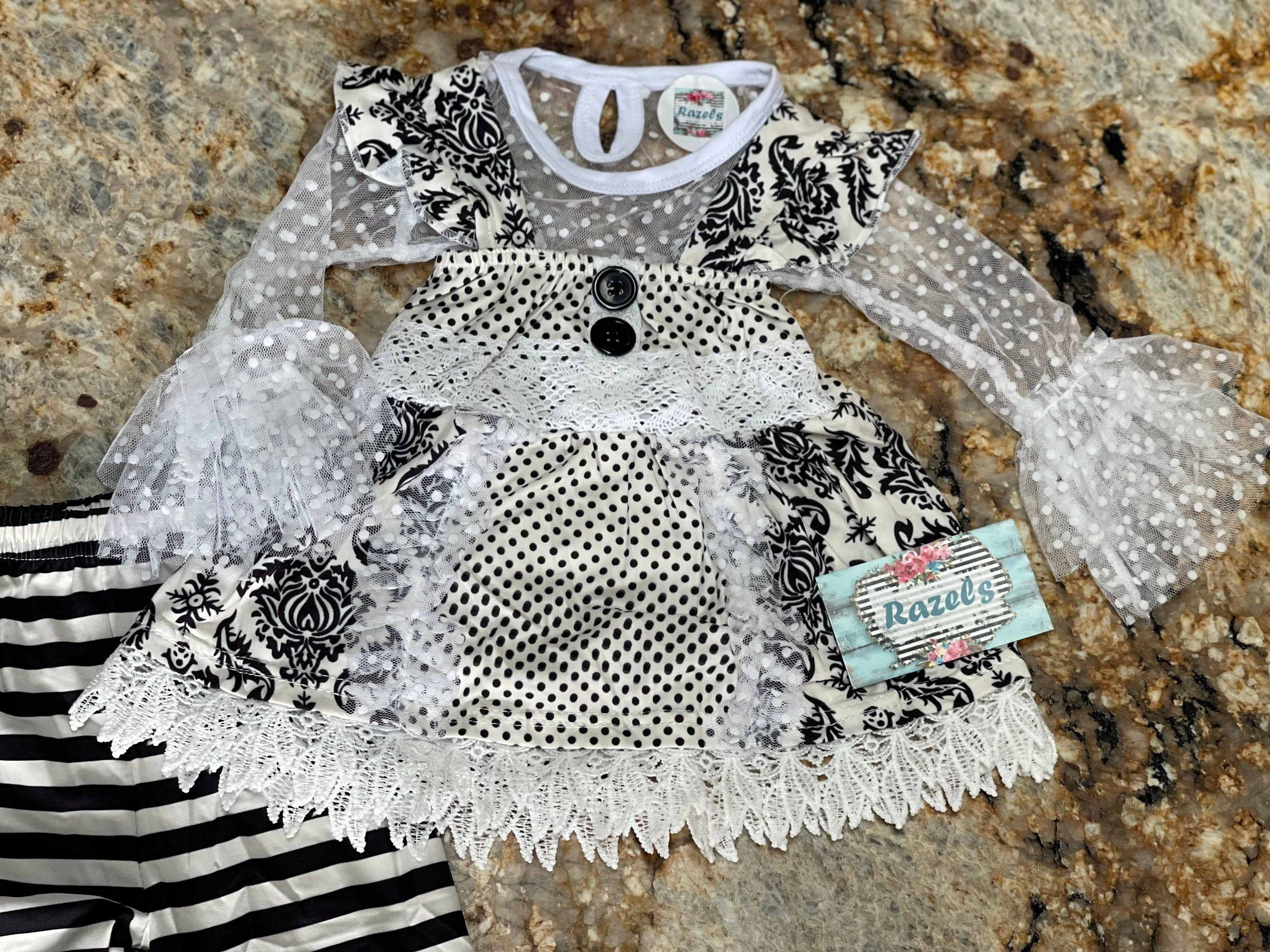 This 3-piece dressy lace outfit for girls includes a lace ruffle top, tunic tank with ruffle straps and buttons, and lace pants with an elastic waist and ruffle ankle details. Outfit is a vintage-inspired black and white design.