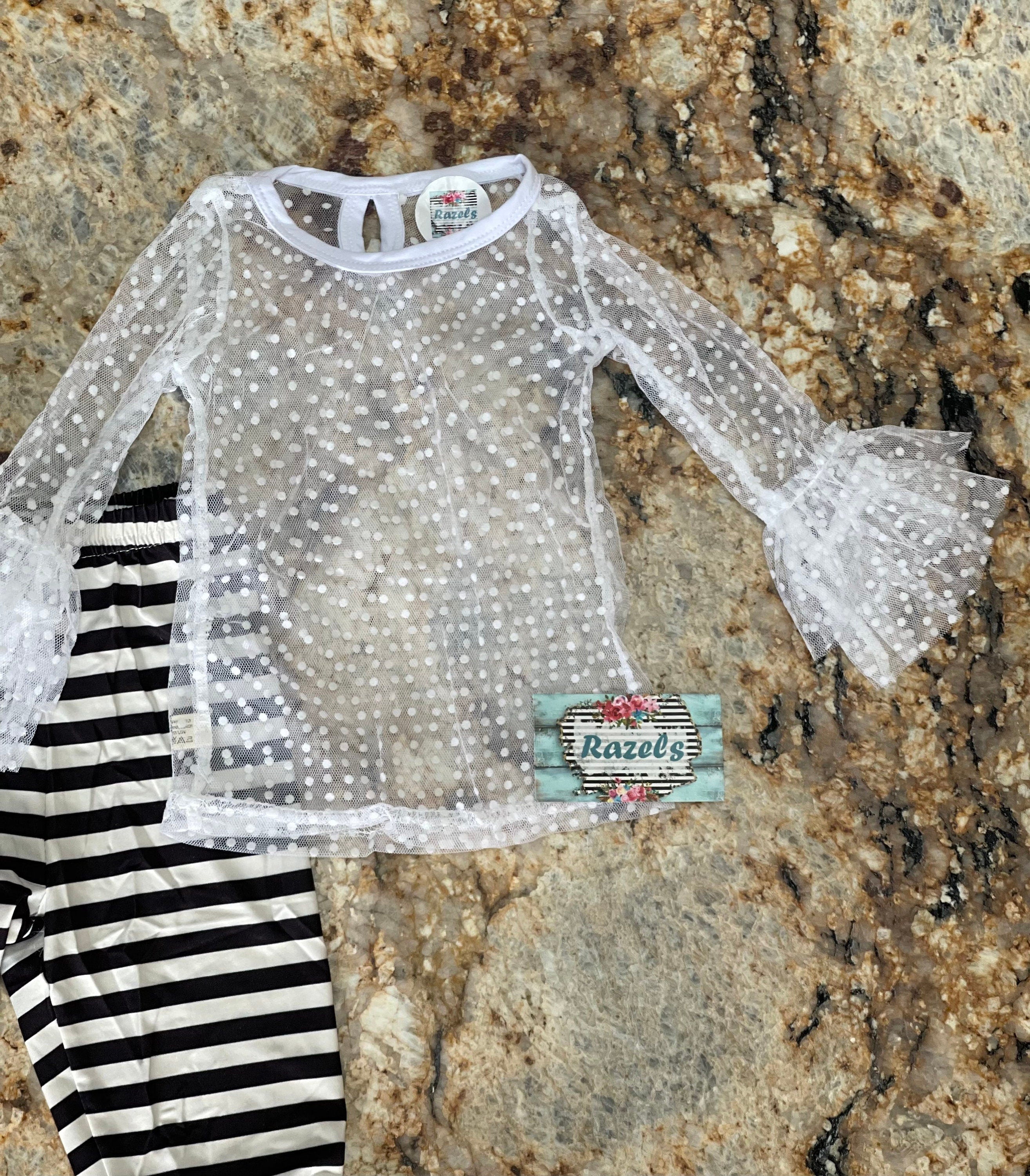 This 3-piece dressy lace outfit for girls includes a lace ruffle top, tunic tank with ruffle straps and buttons, and lace pants with an elastic waist and ruffle ankle details. Outfit is a vintage-inspired black and white design.