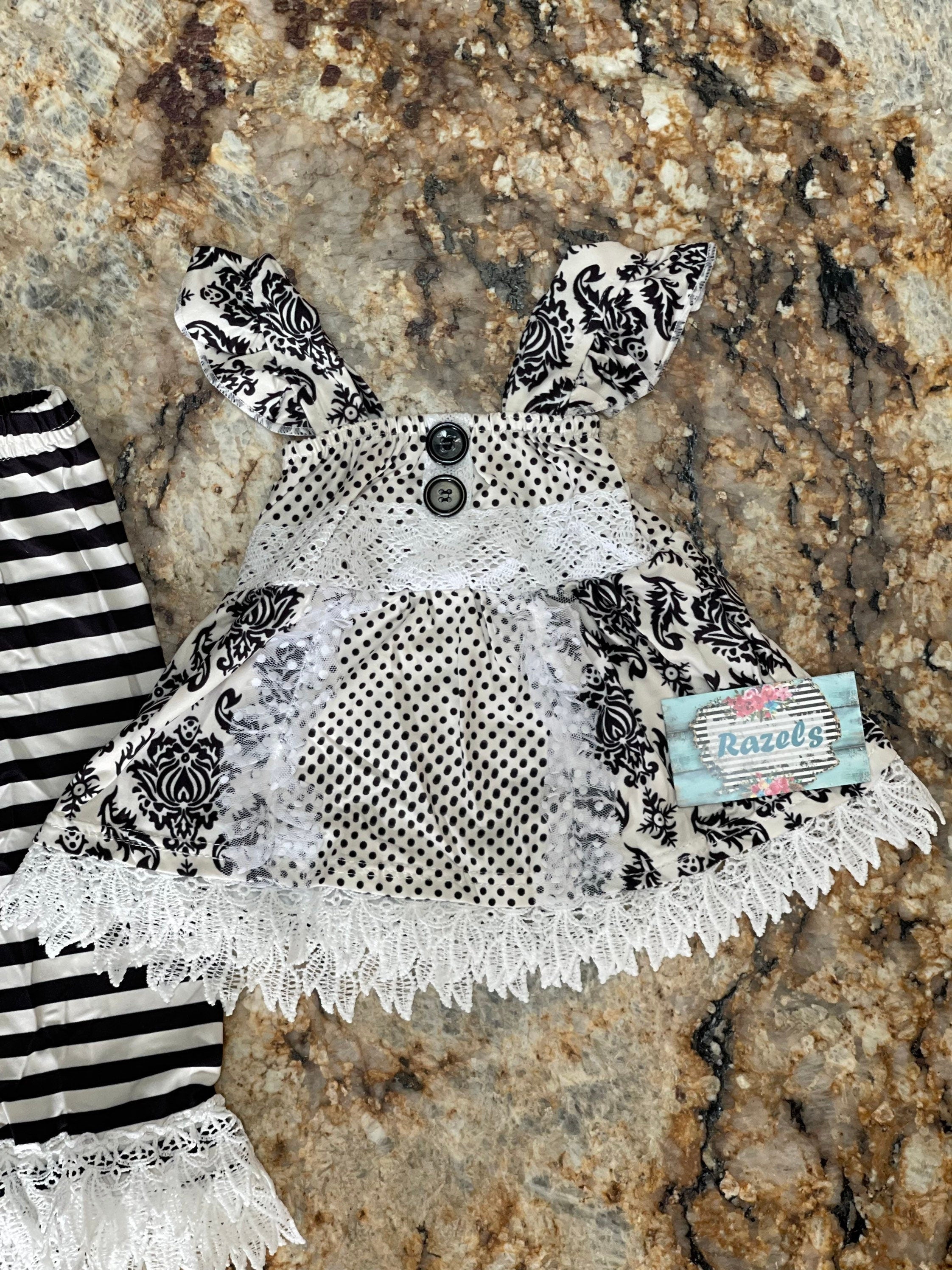 This 3-piece dressy lace outfit for girls includes a lace ruffle top, tunic tank with ruffle straps and buttons, and lace pants with an elastic waist and ruffle ankle details. Outfit is a vintage-inspired black and white design.