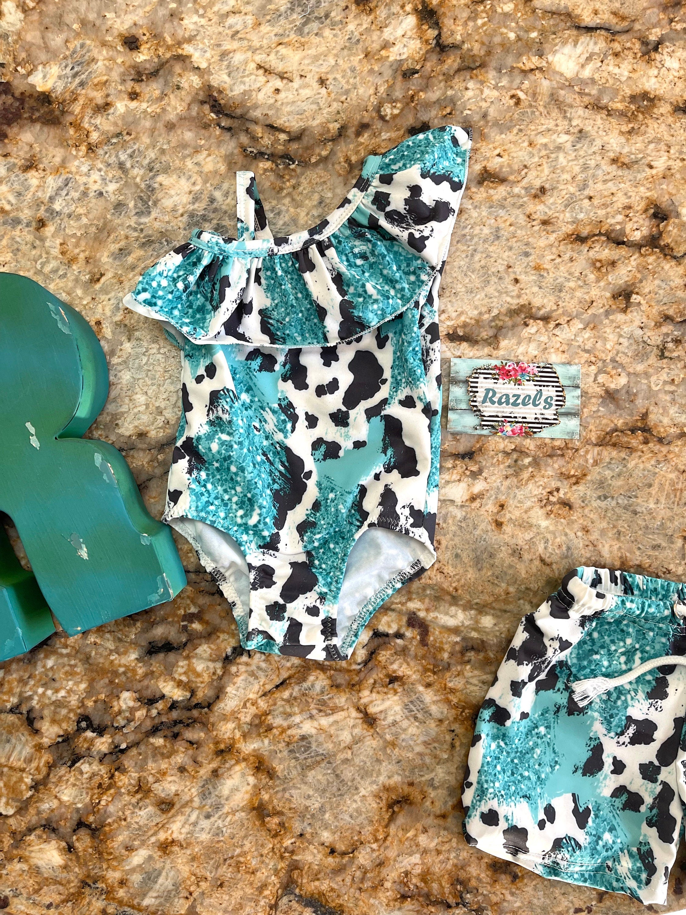 Western Sibling Swimsuits – Turquoise & Black and White Cow Print Matching Swimwear Made from turquoise and black and white cow print fabric, the ruffled one-piece for girls and comfortable swim trunks for boys create the perfect coordinated look.