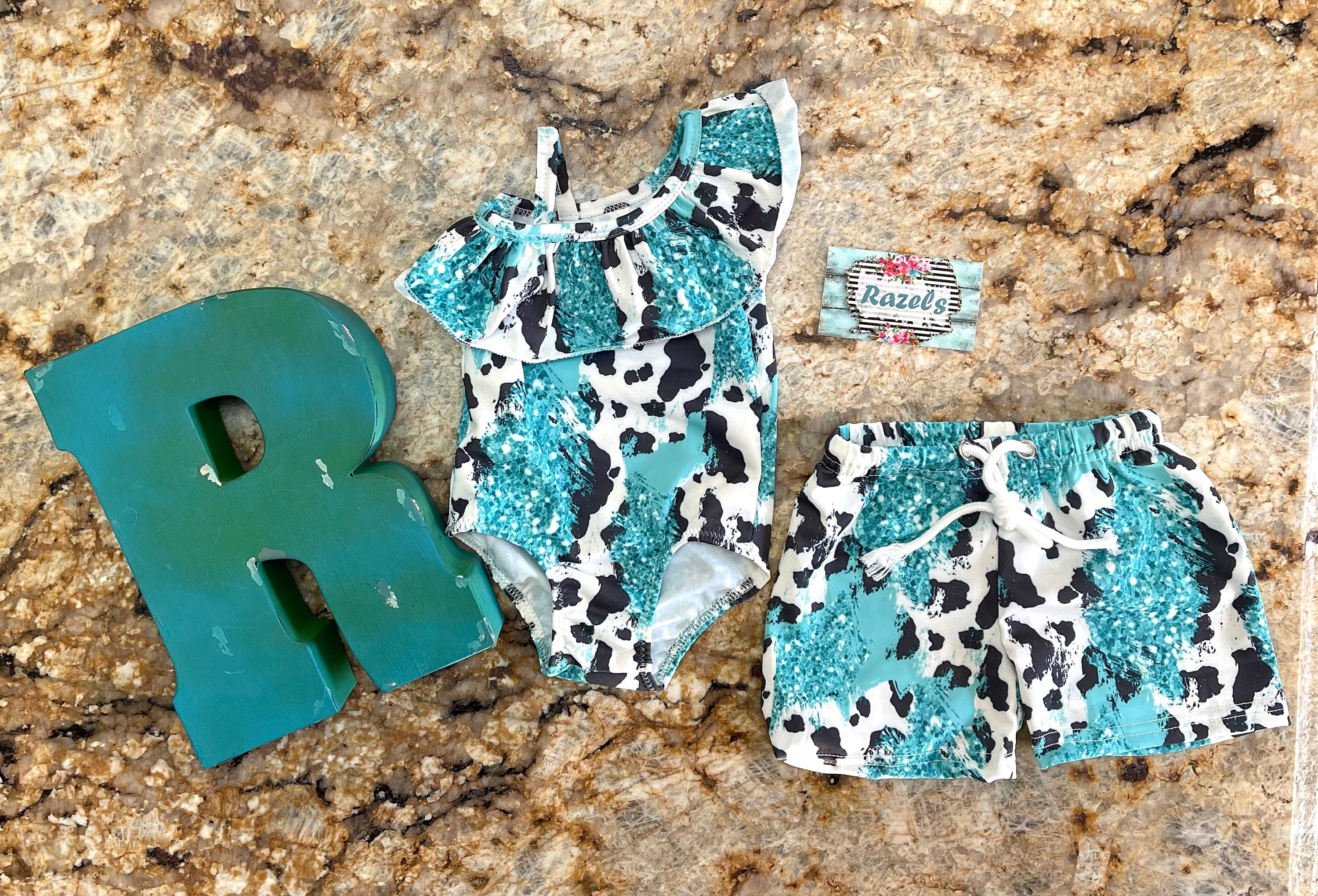 Western Sibling Swimsuits – Turquoise & Black and White Cow Print Matching Swimwear Made from turquoise and black and white cow print fabric, the ruffled one-piece for girls and comfortable swim trunks for boys create the perfect coordinated look.