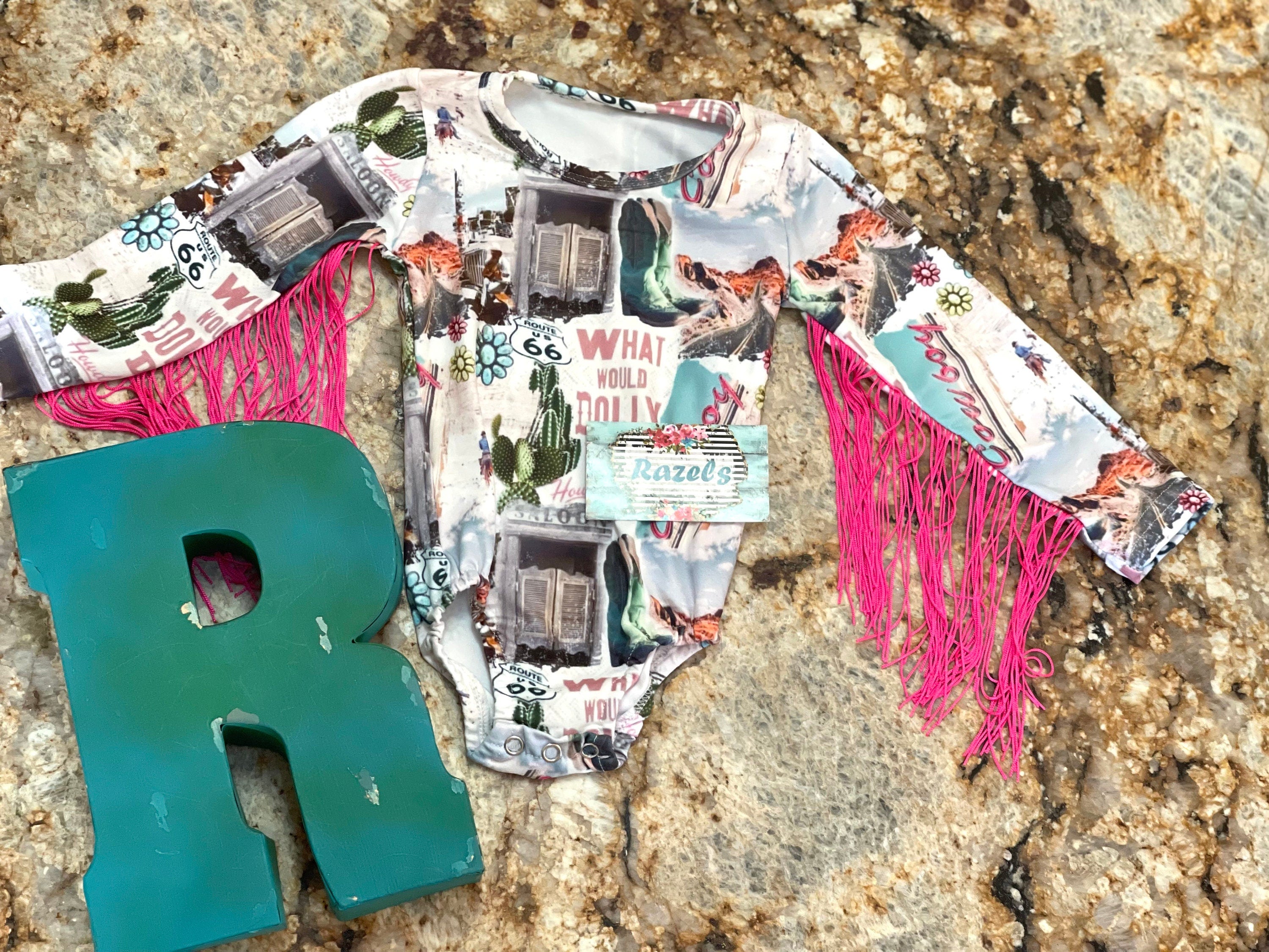 Get ready to dazzle with our adorable What Would Dolly Do? Cowgirl Shirt & Fringe Bodysuit. 
 The button-up shirt features a bold Western-inspired design, while the fringe bodysuit adds flair in vibrant pink. Shop Razels for Girls Western Wear