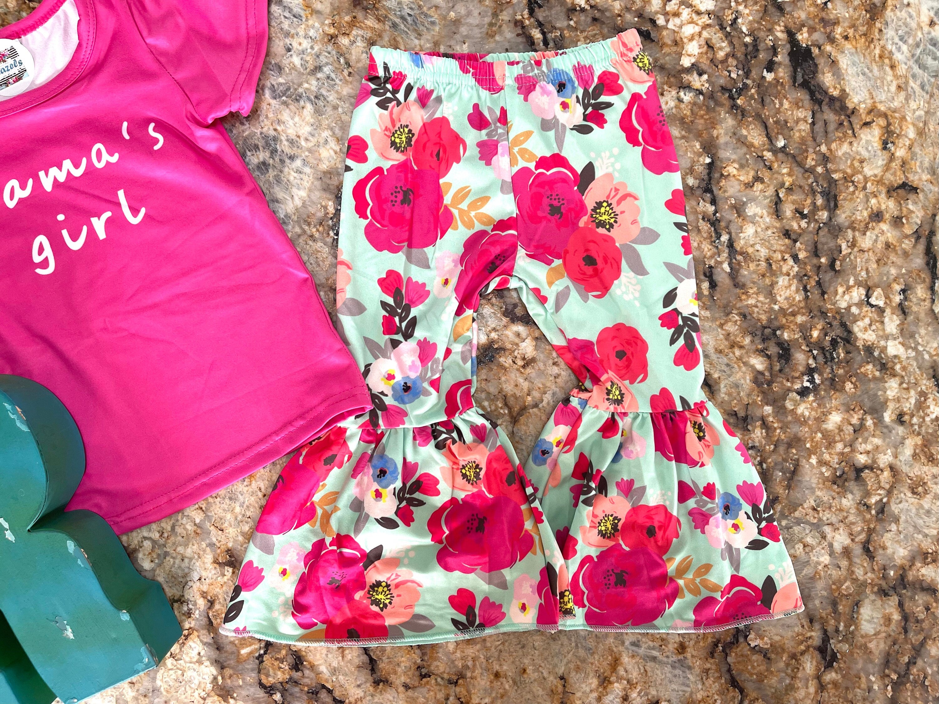 Mama&#39;s Girl Bell Bottom Outfit featuring a hot pink t-shirt with Mama&#39;s Girl proudly scrolled across the front. The flower bell bottoms are so fun and bright with shades of pink against a mint green background.