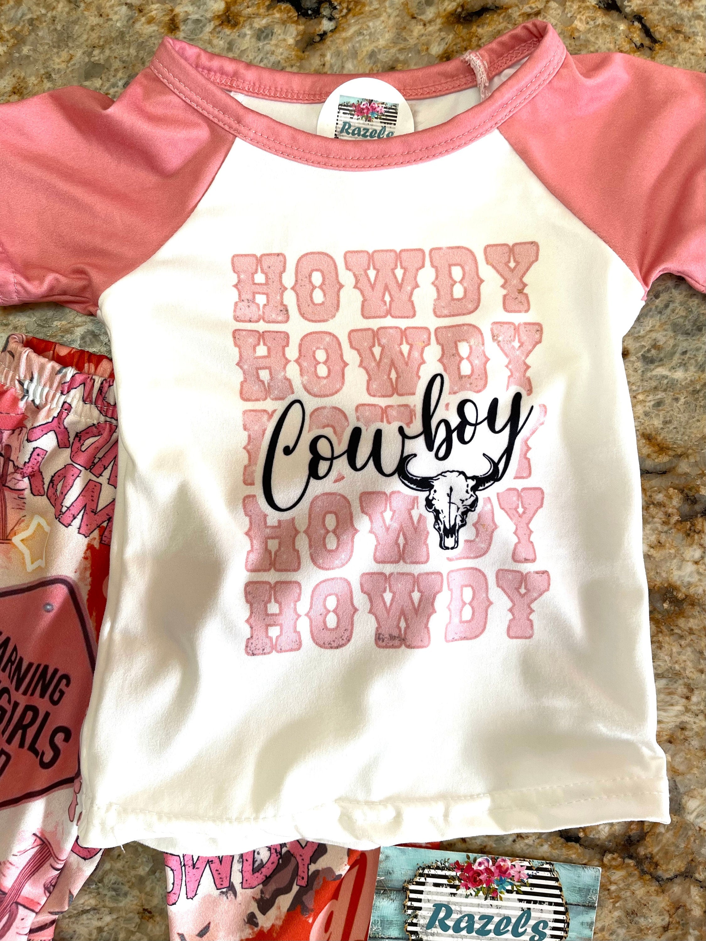 girls HowdyCowboy Bell Bottom Outfit. T-shirt is baseball style with short pink sleeves and Howdy Cowboy scrolled across the front. Pants are pink bell bottom with Howdy, Warning Cowgirl ahead, stars,horses, cowprint western print