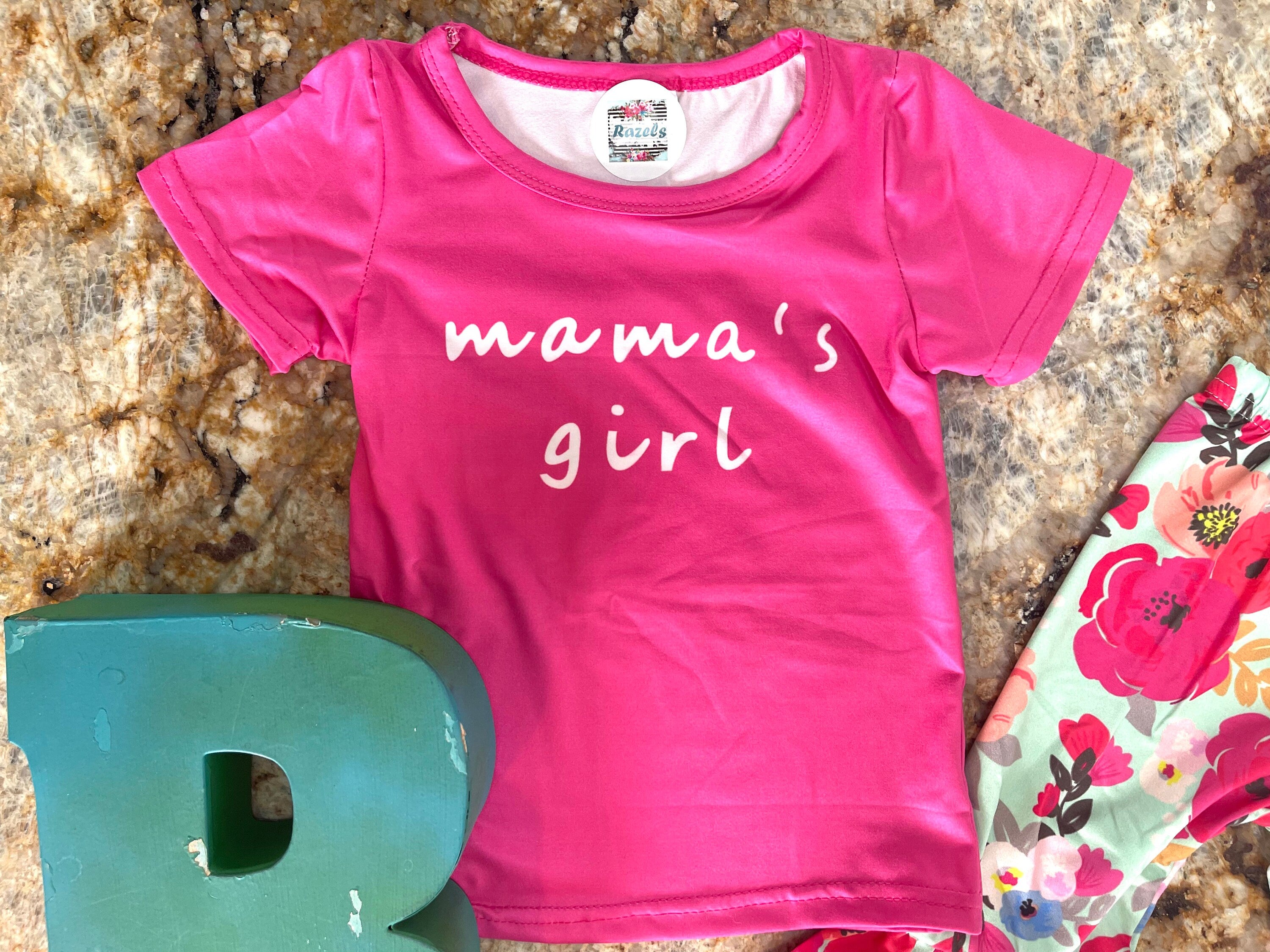 Mama&#39;s Girl Bell Bottom Outfit featuring a hot pink t-shirt with Mama&#39;s Girl proudly scrolled across the front. The flower bell bottoms are so fun and bright with shades of pink against a mint green background.