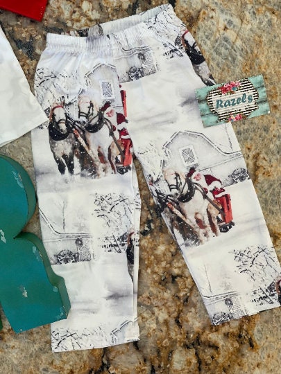Family White Christmas Pajamas feature Santa Claus at the reins of a horse-drawn sleigh, pulling away from a vintage barn on a snowy winter day. The top has coordinating red raglan sleeves, and the bottoms feature a festive Santa print all over