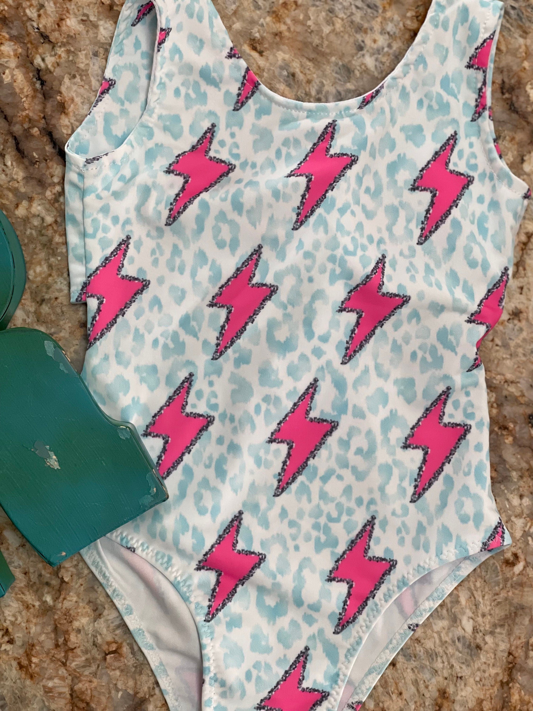 Pink Lightning Bolt One- piece Swimsuit is a Turquoise Cheetah Print One-Piece swimsuit featuring a striking pink lightning bolts and turquoise cheetah print design with a tie-back detail. Available in sizes 0/3 months to 8/9 years. Ships FREE $35+