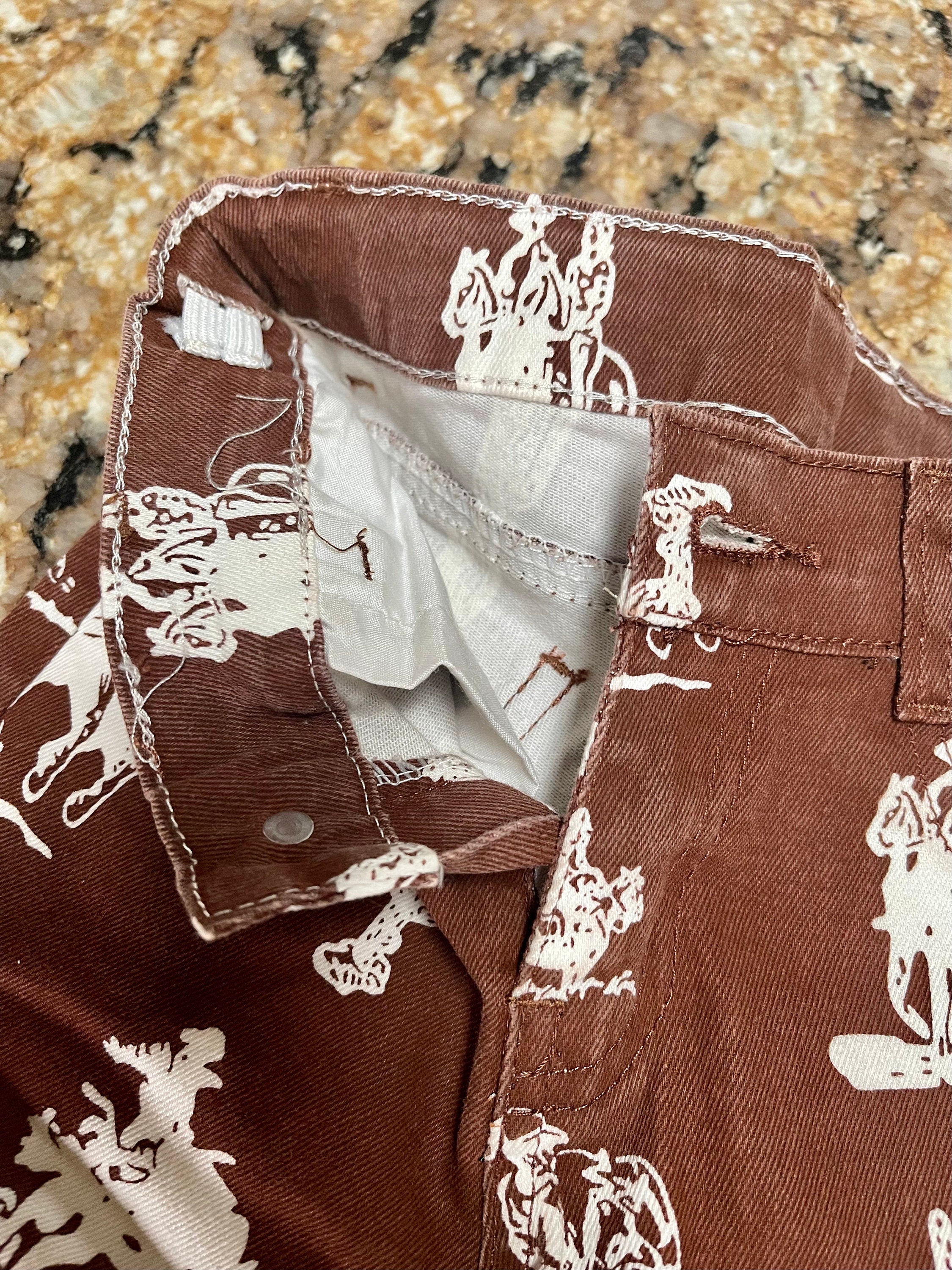 Brown Vintage Cowboy Bell Bottom Jeans featuring a vintage cowboy print, adjustable waistband, functioning pockets, and frayed bells. Styled with a matching Mama&#39;s Cowgirl T-shirt. Ideal for dressing up or down, perfect for little cowgirls.&quot;
