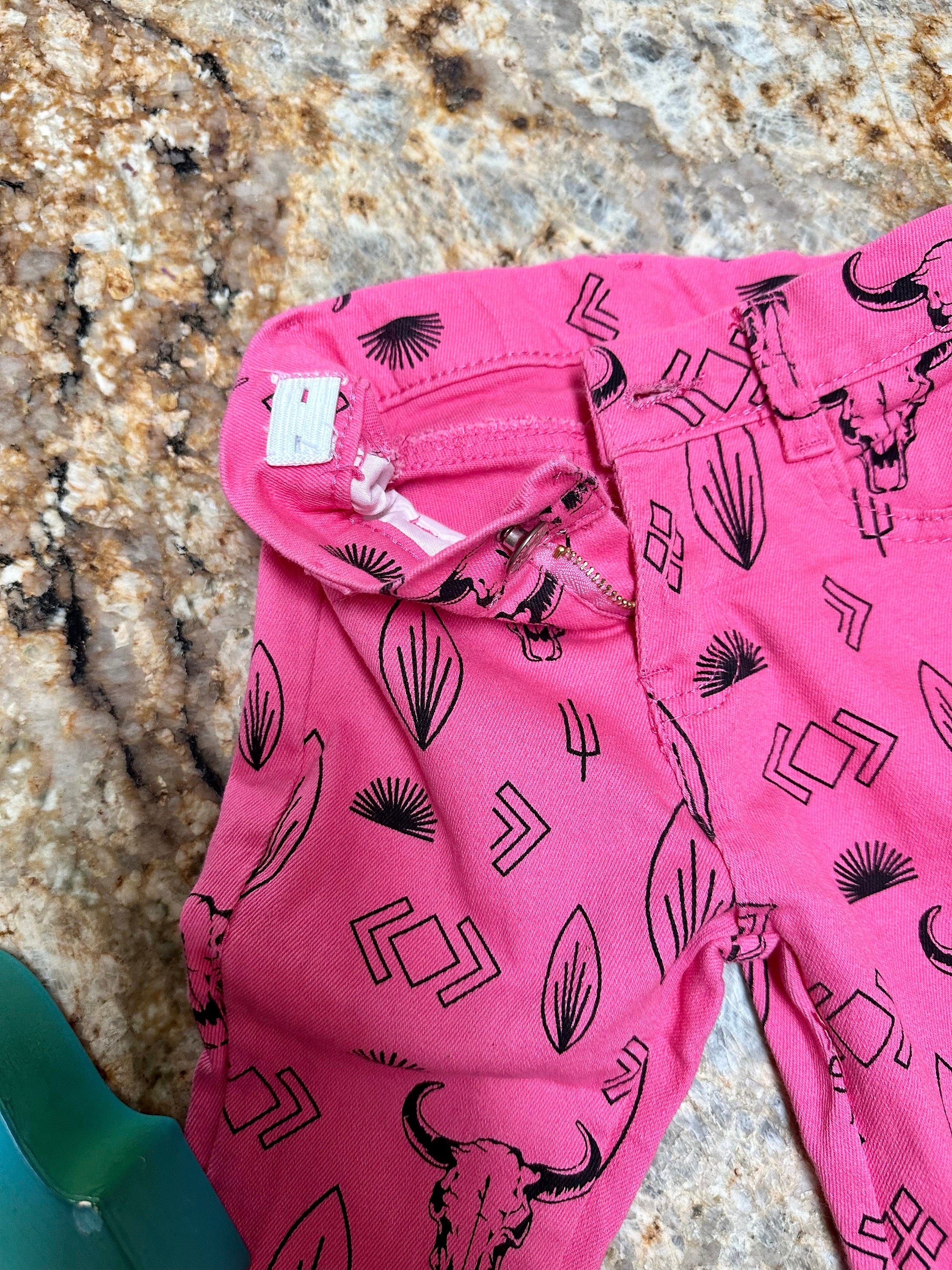 Girls Western Hot Pink Jeans. Jeans feature black steerheads, arrows, and cacti in an awesome western motif. Jeans have an adjustable waistband, pockets, and a frayed bell bottom hem.