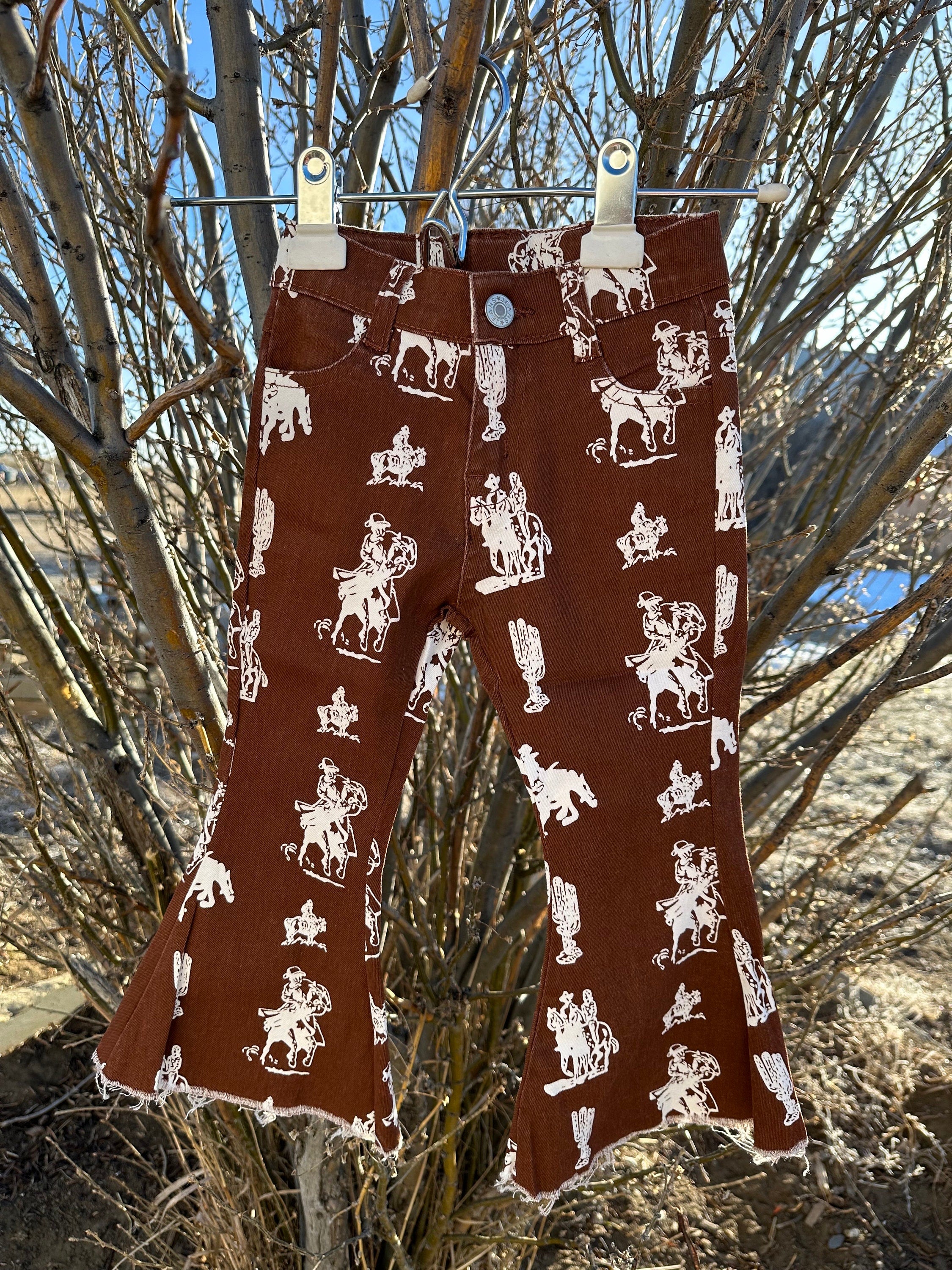 Brown Vintage Cowboy Bell Bottom Jeans featuring a vintage cowboy print, adjustable waistband, functioning pockets, and frayed bells. Styled with a matching Mama&#39;s Cowgirl T-shirt. Ideal for dressing up or down, perfect for little cowgirls.&quot;