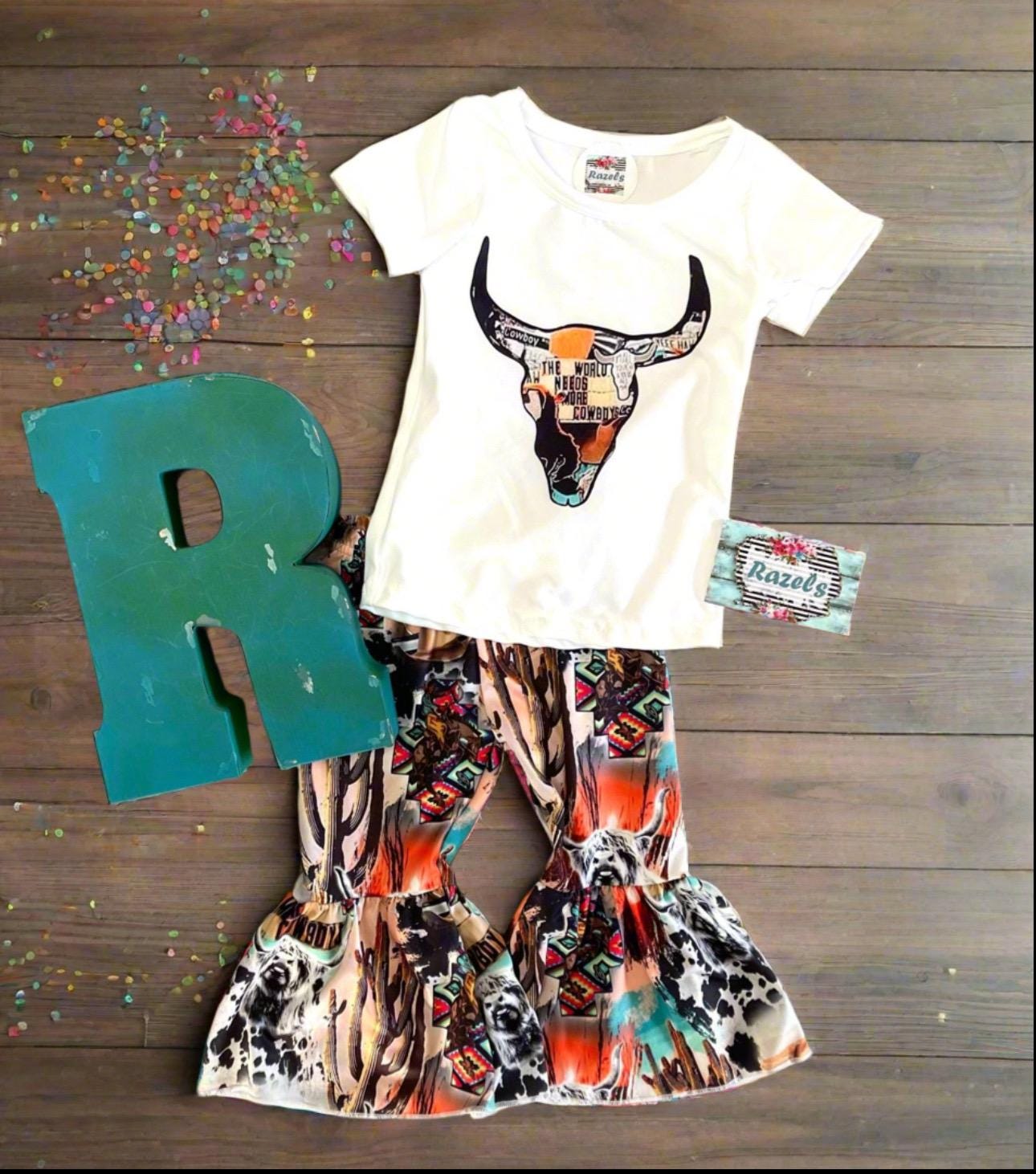 The WorldNeedsMore Cowboys Bell Bottom Outfit, bell bottom pants are a mosaic of Scottish highlander cows, cowprints and cactus. Tshirt features a mosaic inside a cow skull stating the world needs more Cowboys