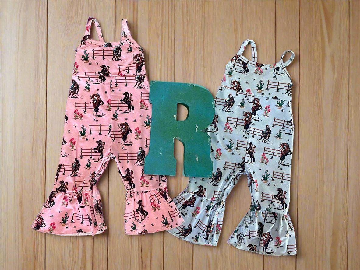 Razels Western Cowgirl Print Jumpsuit in Blue and pink. This fun jumpsuit features a vintage cowgirl print of bucking and rearing horses and their best cowgirls.  Legs have a flare/bell bottom hem and spaghetti strap. An easy-peasy outfit!