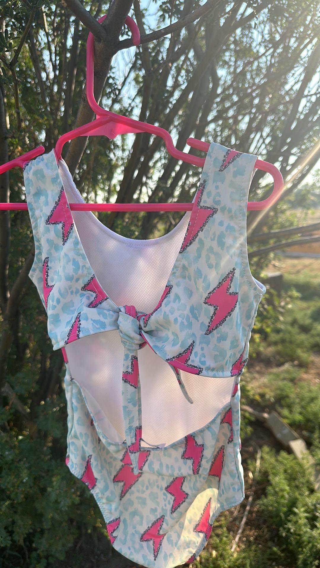 Pink Lightning Bolt One- piece Swimsuit is a Turquoise Cheetah Print One-Piece swimsuit featuring a striking pink lightning bolts and turquoise cheetah print design with a tie-back detail. Available in sizes 0/3 months to 8/9 years. Ships FREE $35+