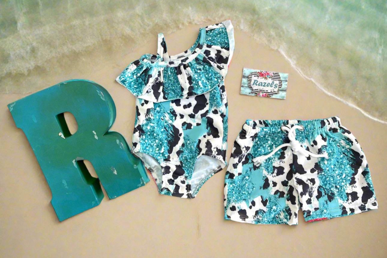 Western Sibling Swimsuits – Turquoise & Black and White Cow Print Matching Swimwear Made from turquoise and black and white cow print fabric, the ruffled one-piece for girls and comfortable swim trunks for boys create the perfect coordinated look.