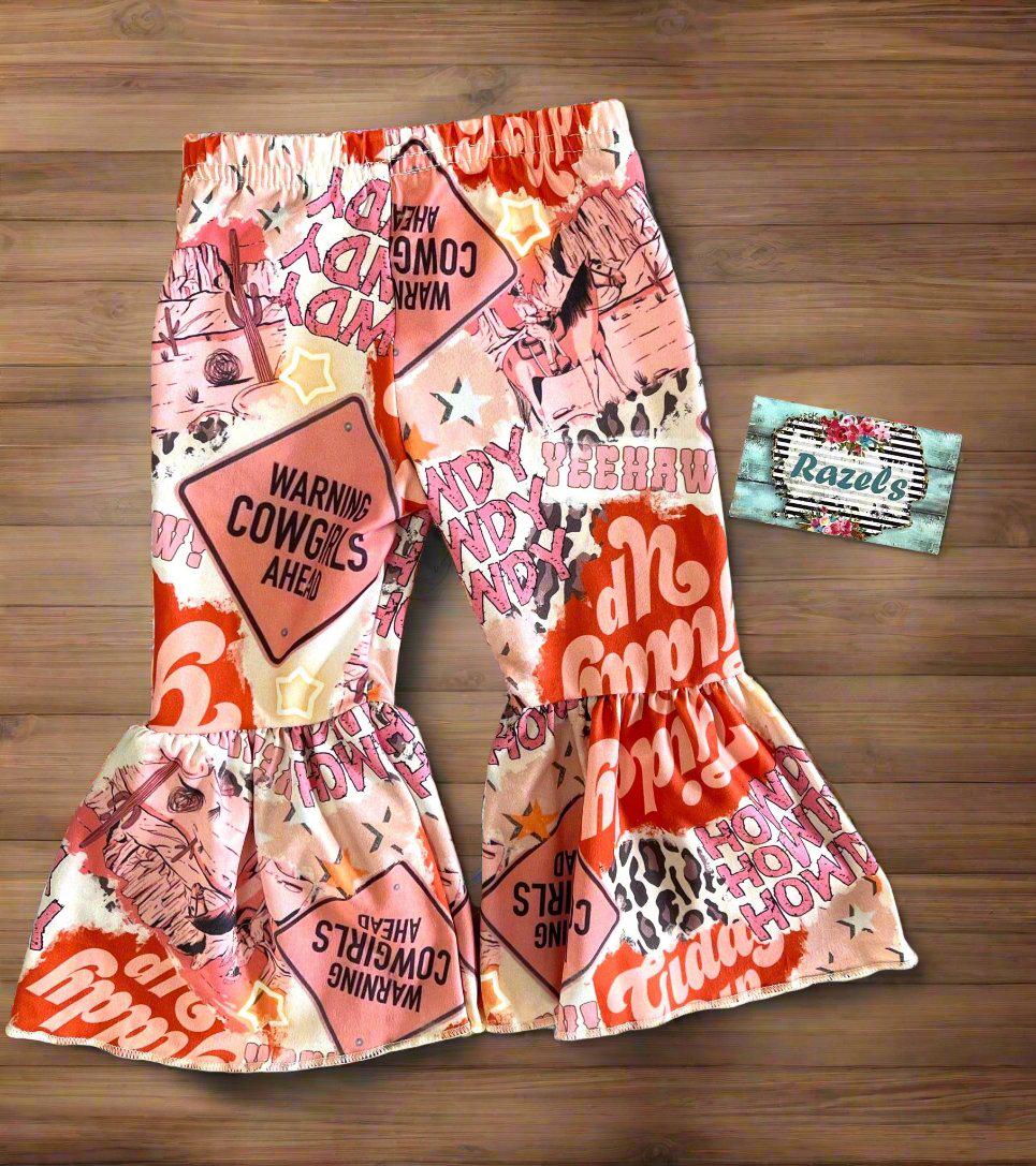 girls HowdyCowboy Bell Bottom Outfit. T-shirt is baseball style with short pink sleeves and Howdy Cowboy scrolled across the front. Pants are pink bell bottom with Howdy, Warning Cowgirl ahead, stars,horses, cowprint western print