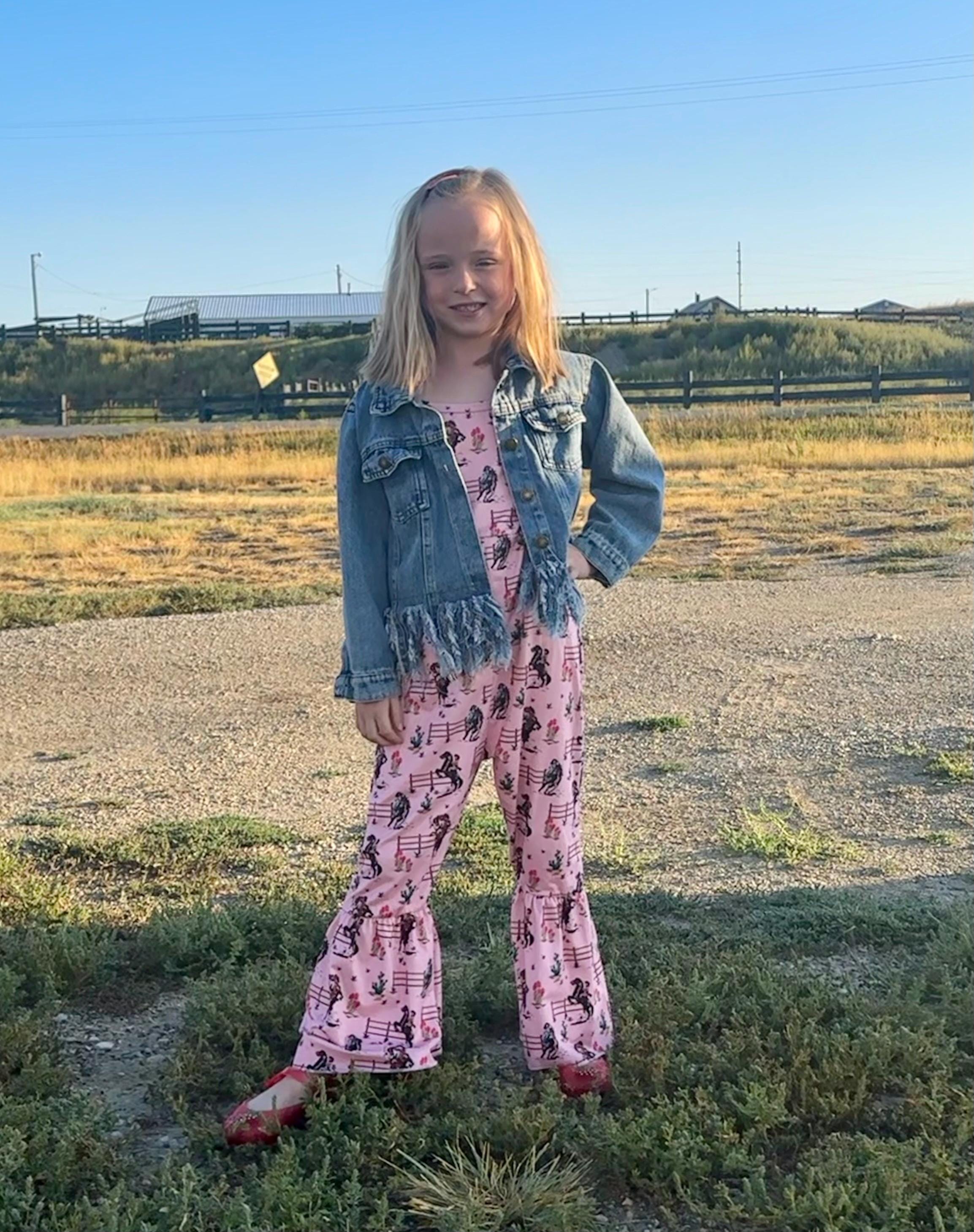 Jernie modeling Western Cowgirl Print romper in pink. This fun jumpsuit features a vintage cowgirl print of bucking and rearing horses and their best cowgirls.  Legs have a flare/bell bottom hem and spaghetti strap. An easy-peasy outfit!