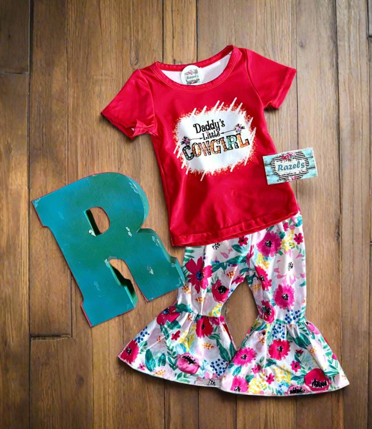 Daddy’s Little Cowgirl Bell Bottom Outfit perfect for Father&#39;s day and all Spring long! This Girls Western T-Shirt & Flower Bell Bottom Pants Set features a red &#39;Daddy&#39;s Little Cowgirl&#39; graphic T-shirt paired with vibrant flower pants bell-bottom style! Ships FREE with $35+ purchase